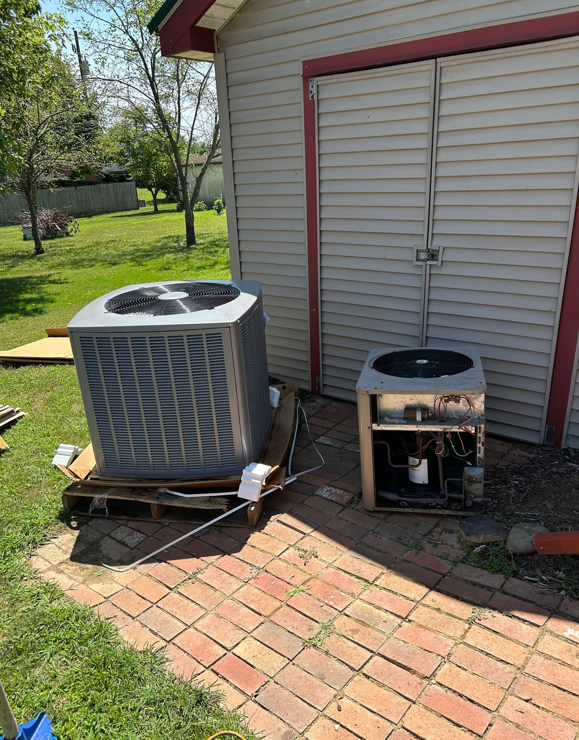 Two industrial HVAC units on a raised wooden platform against a tan building; snowing.