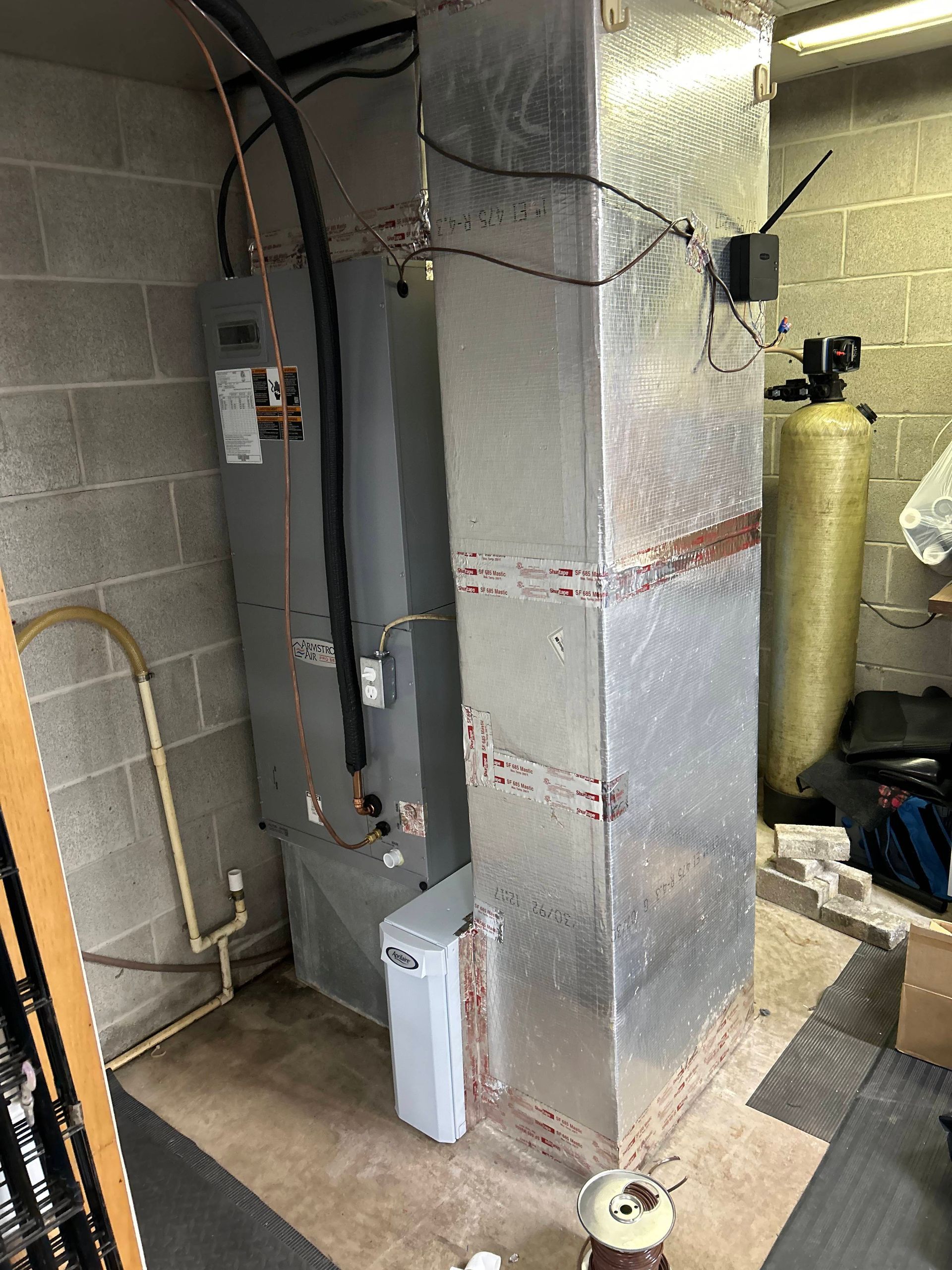 Basement utility room with HVAC unit, ductwork, and water softener tanks against cinder block walls.