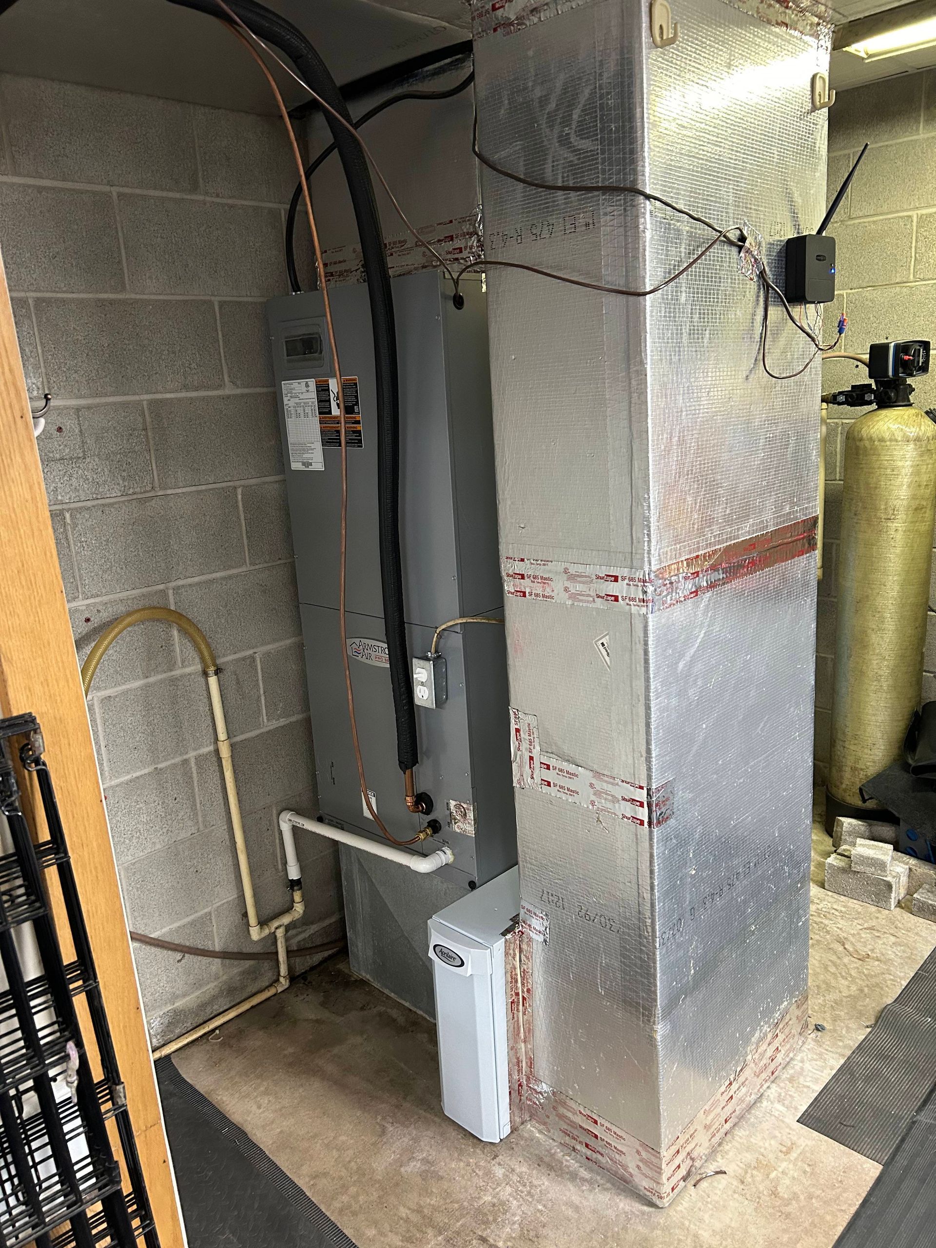 Basement mechanical room with gray HVAC unit, ductwork, pipes, and insulated wall panels.