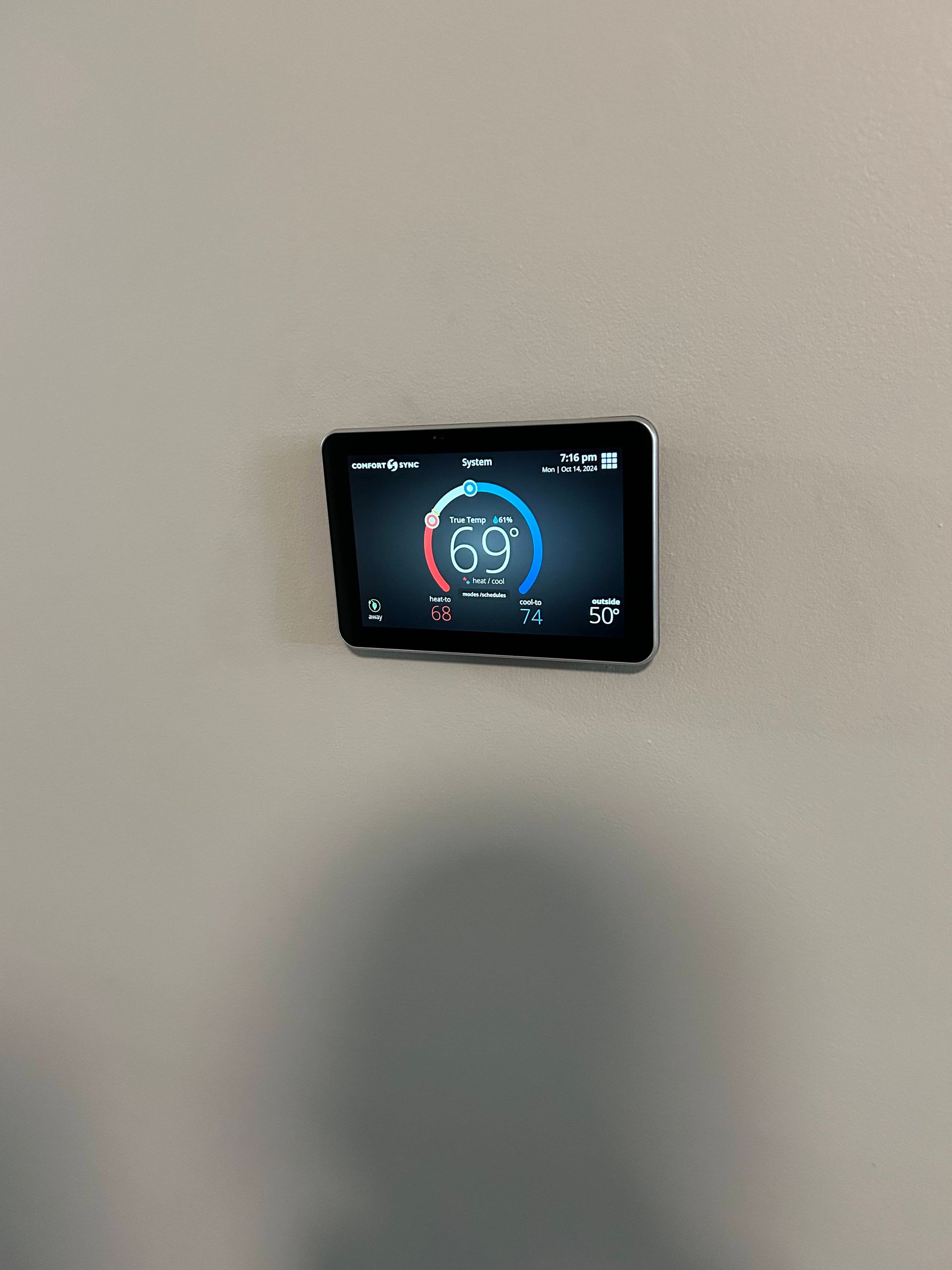Wall-mounted thermostat display with a blue and red circular temperature gauge on a beige wall