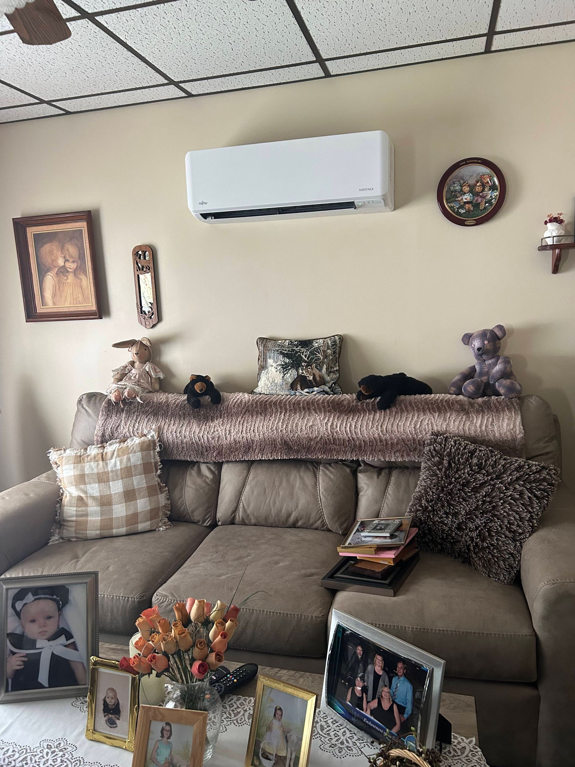 Cozy living room with sectional sofa, wall art, clock, and framed family photos on a table.