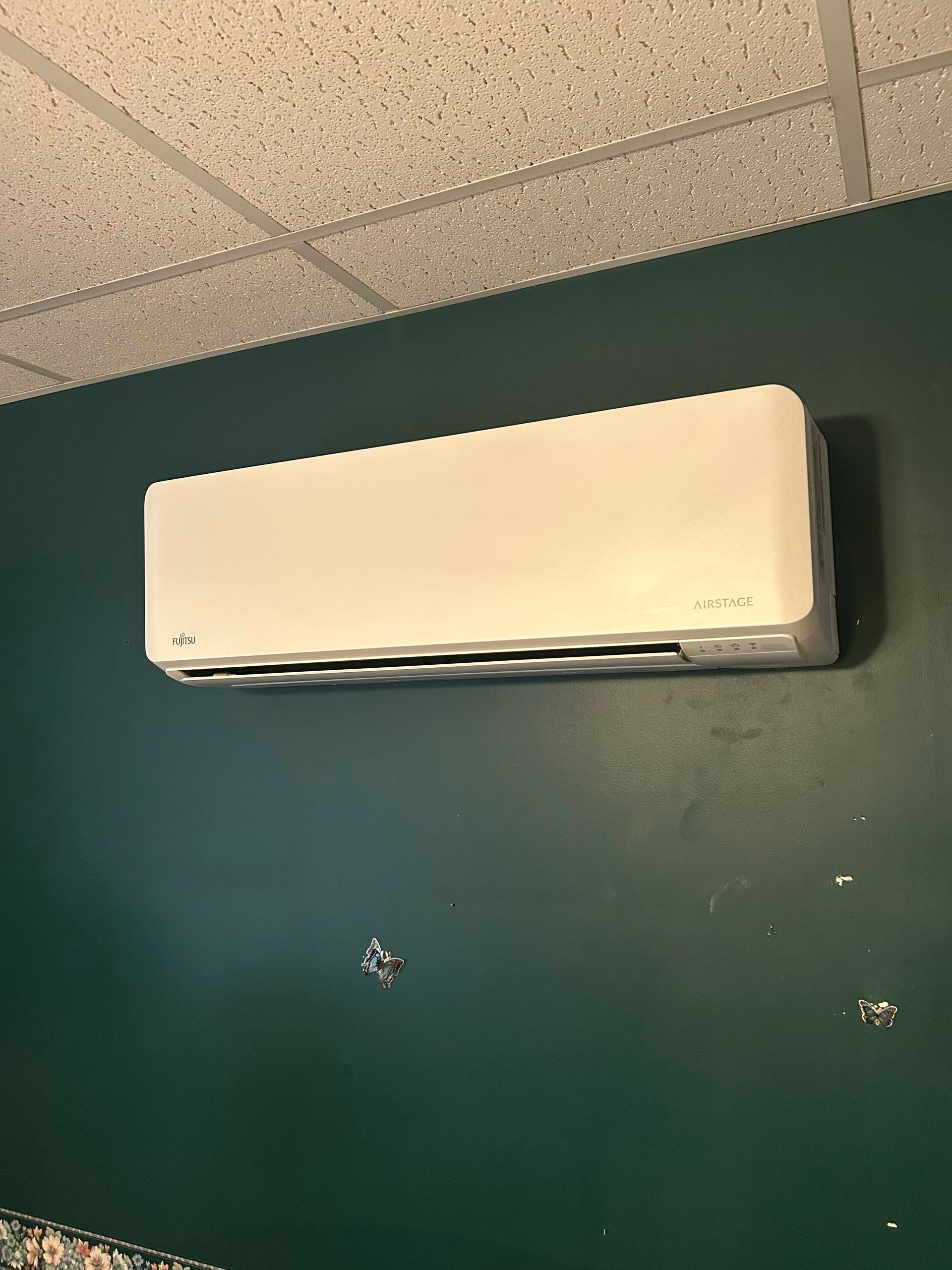 White wall-mounted air conditioner on a dark green wall beneath a drop ceiling.
