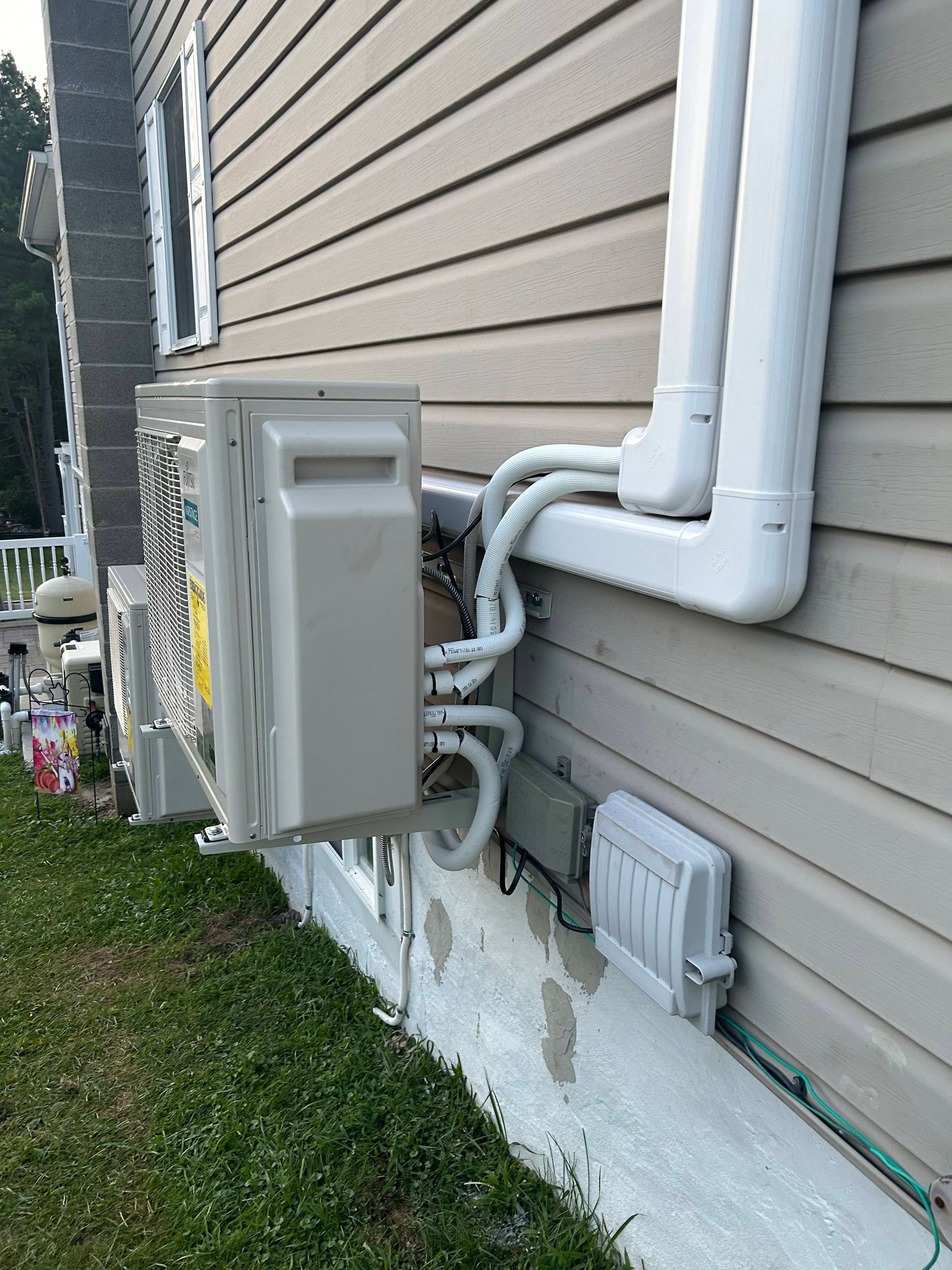 Utility meter and electrical conduit mounted on the side of a beige house near the ground.