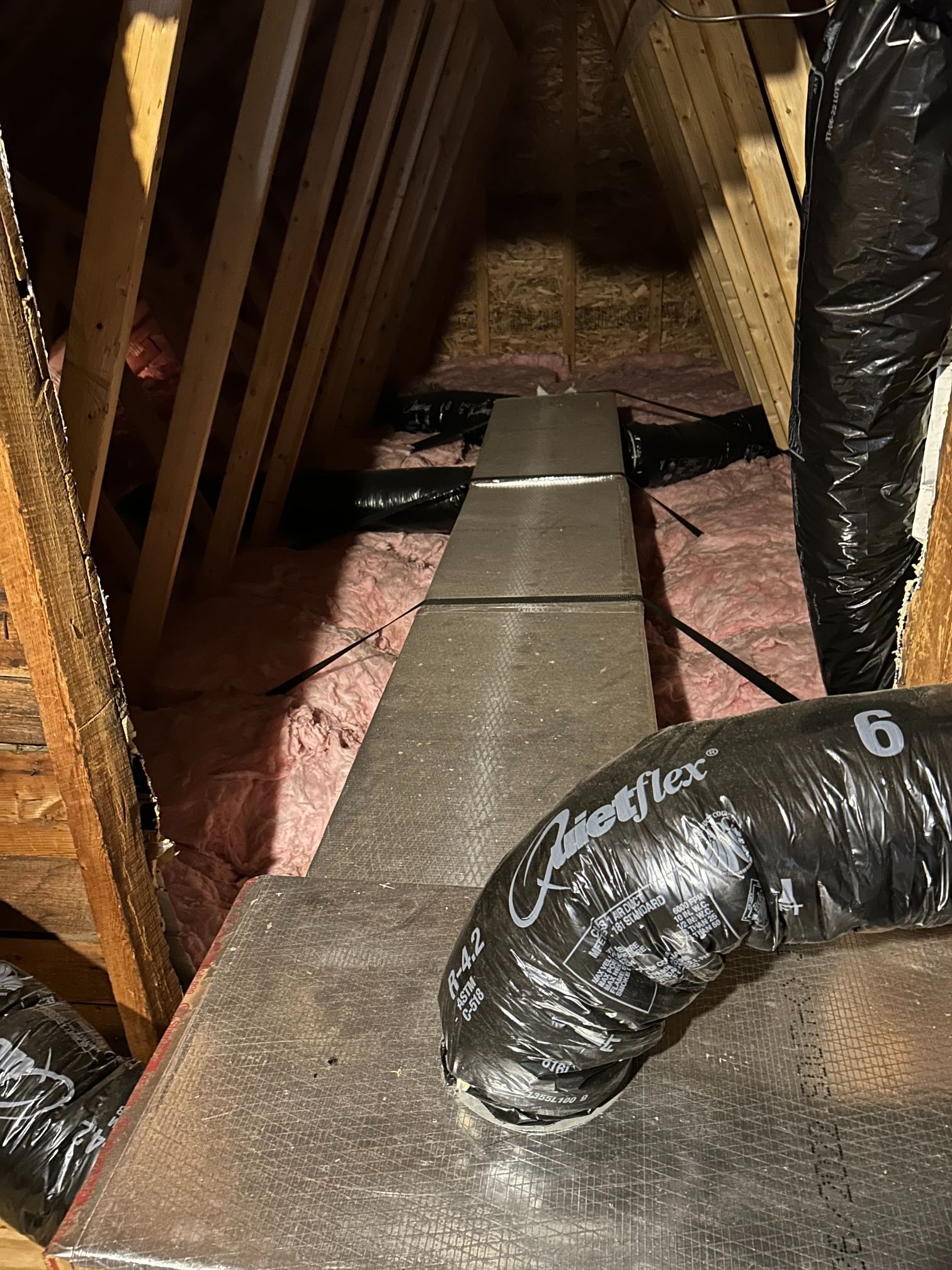 Attic crawlspace with flexible ductwork and insulation along a narrow floor duct track