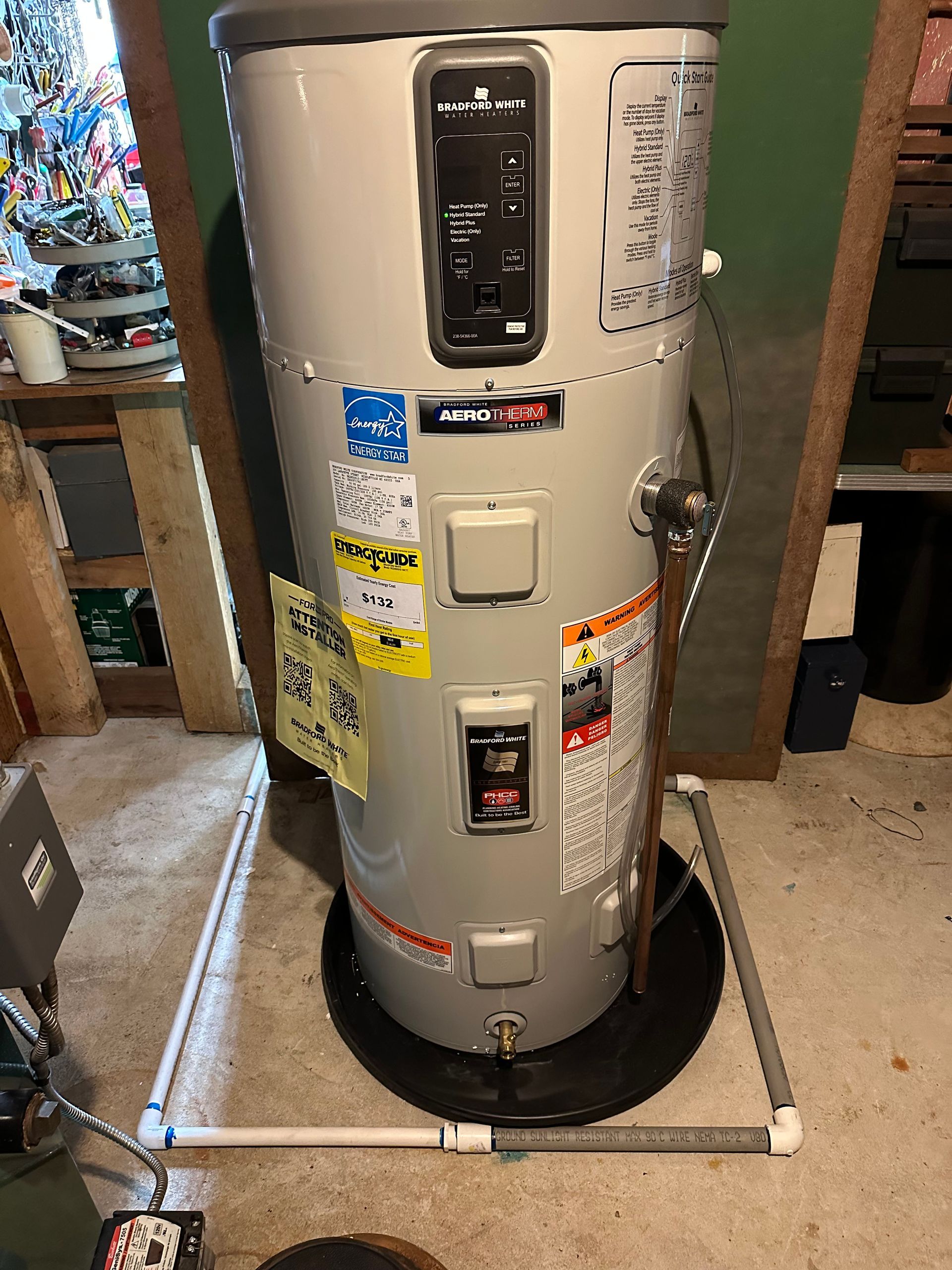 Gray gas water heater in a utility area, with labels, pipes, and a black base stand.