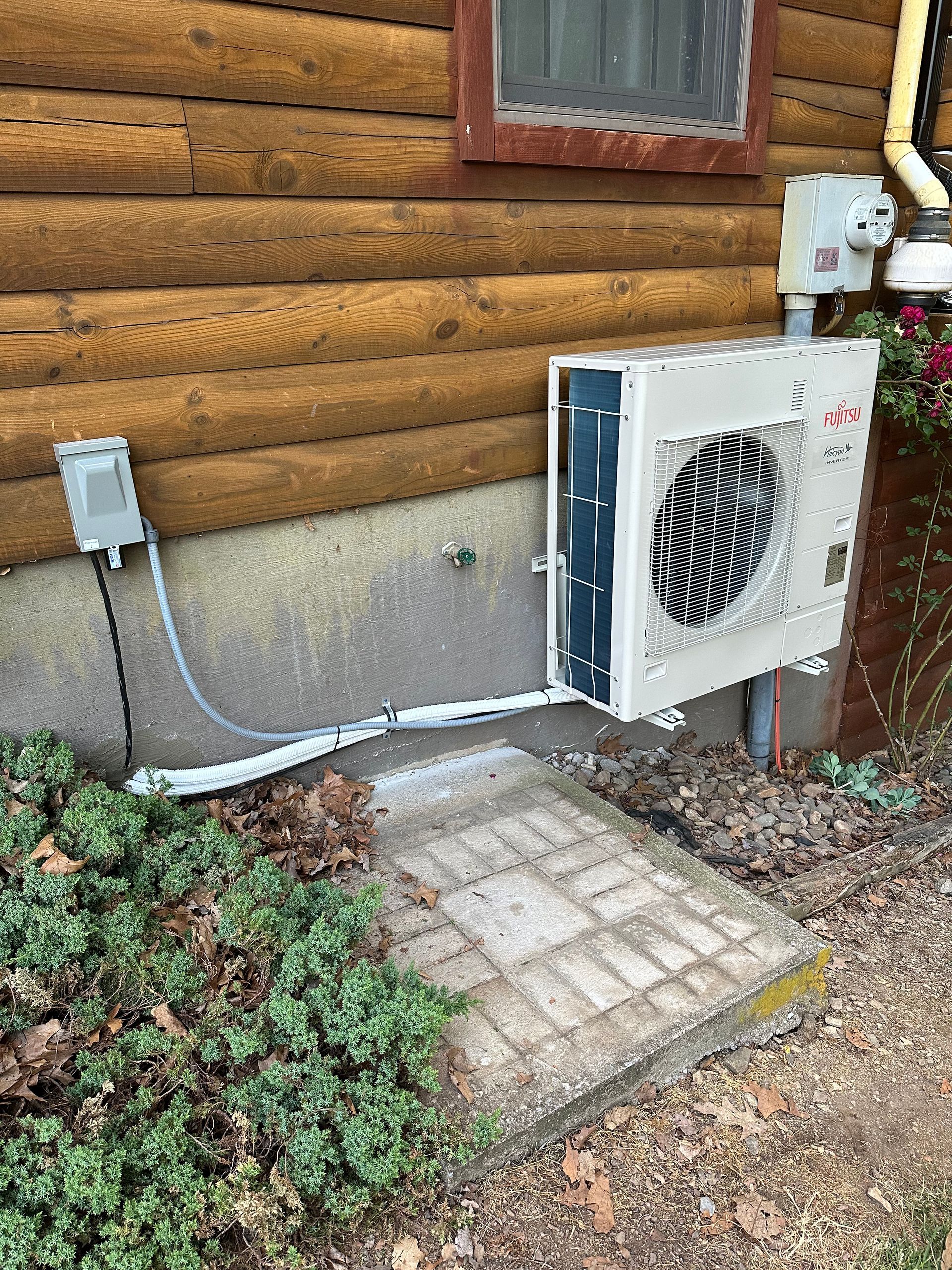 An air conditioning unit is installed near a building's wall, with electrical connections and service tools nearby.