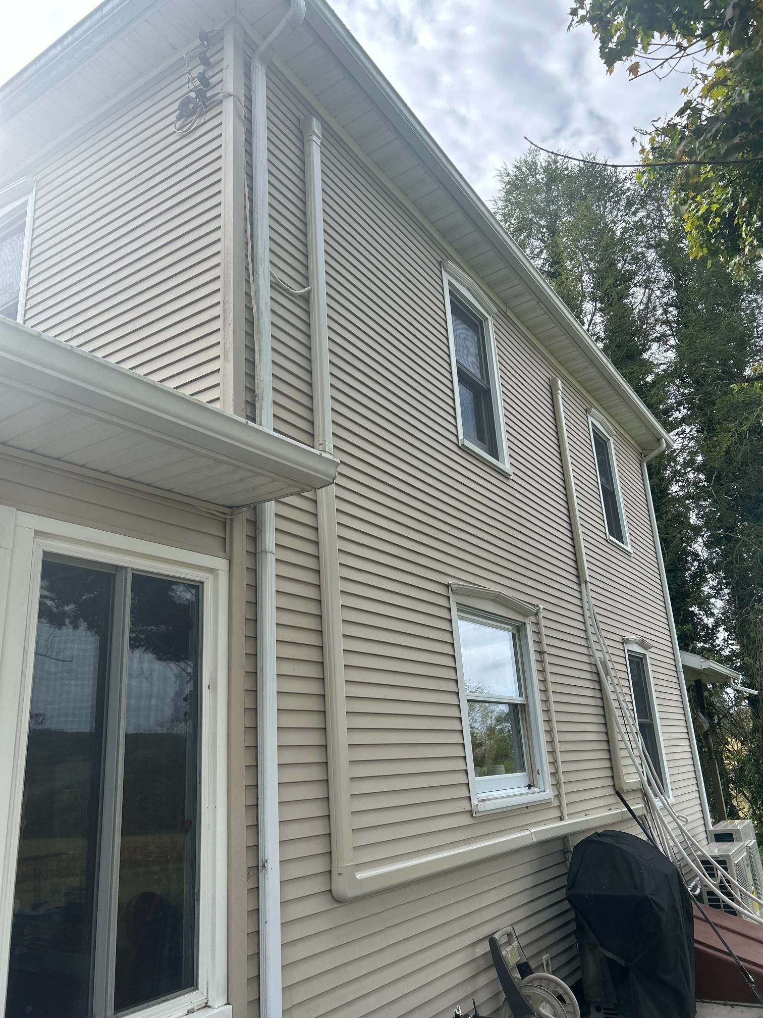 Side view of a beige vinyl-sided house with white trim, windows, and a basement stairway outside.