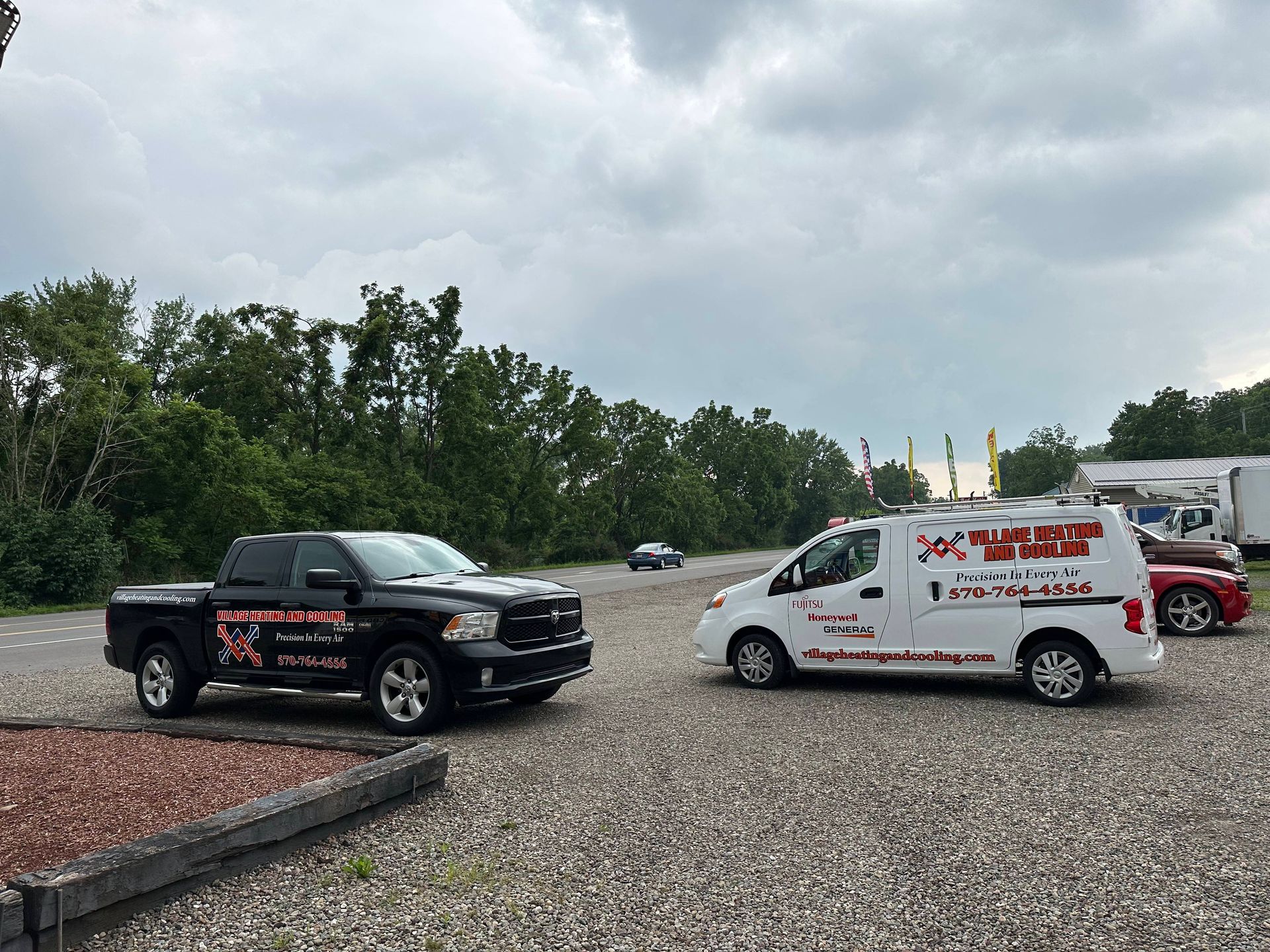 Two tow trucks parked on a gravel lot under cloudy skies, one black and one white.