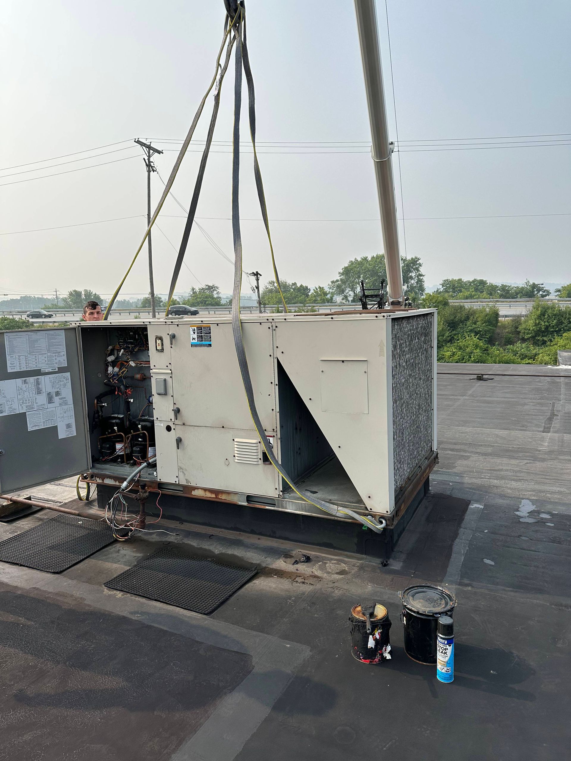 Large industrial generator being lifted by crane onto a rooftop beside a utility pole.