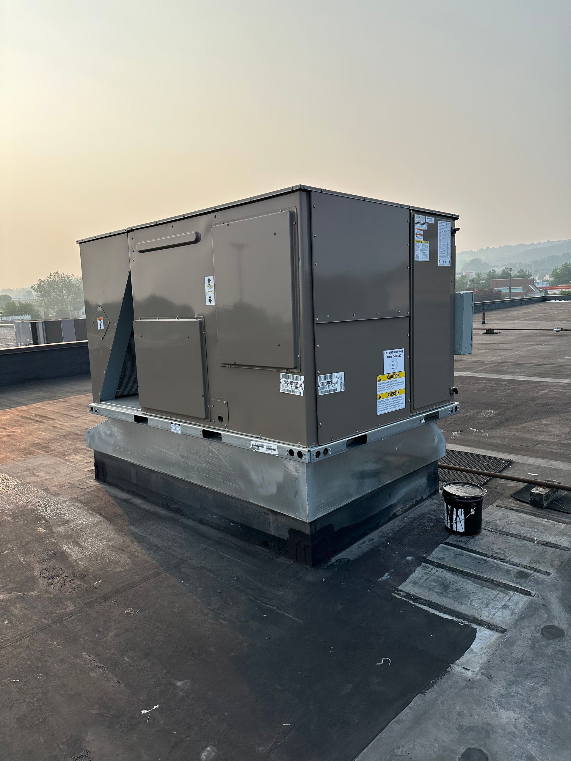 Rooftop HVAC unit on a flat roof. Gray metal box on a concrete base.
