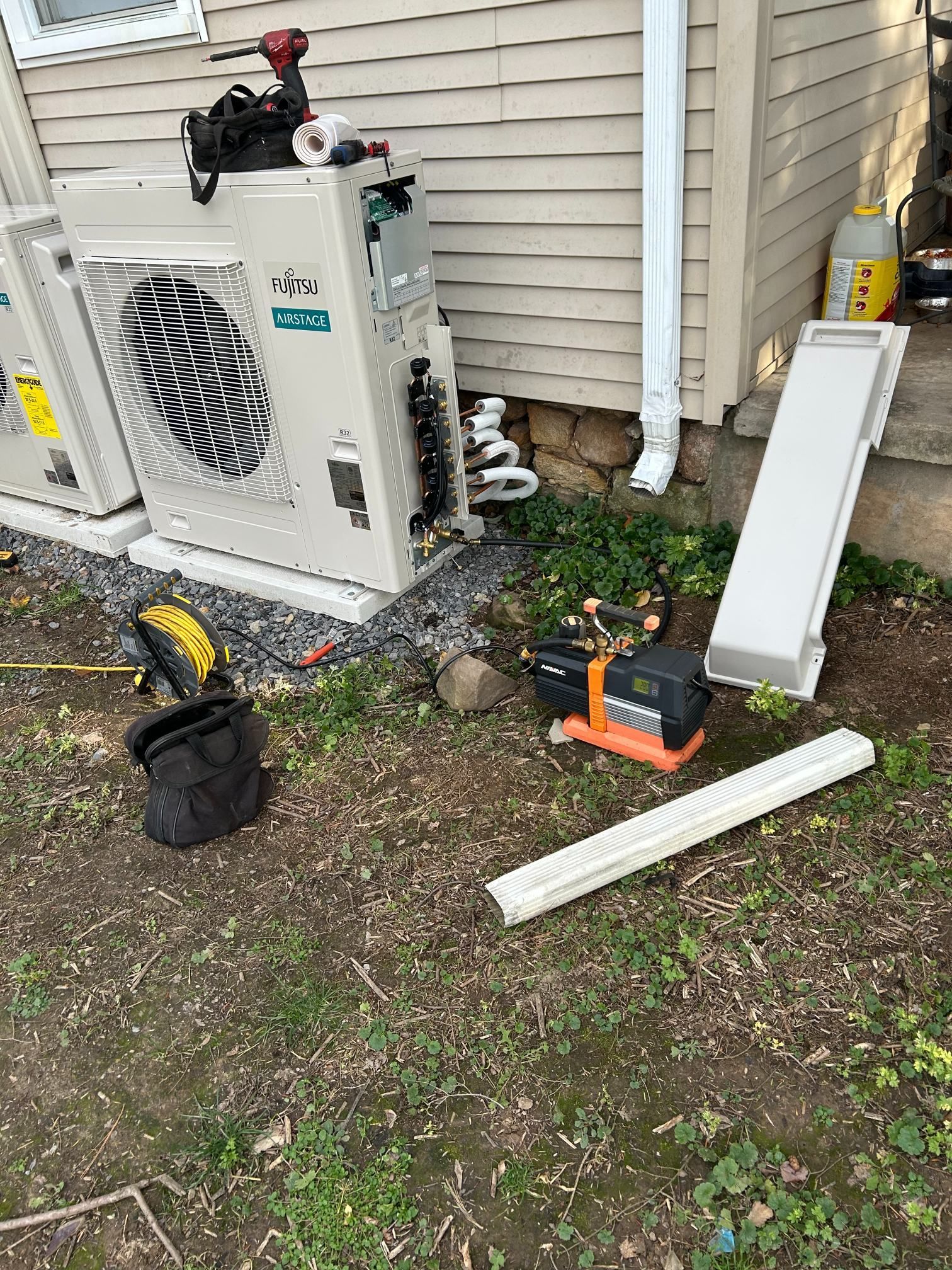 Outdoor HVAC unit beside house with tools, pipes, and debris from repair work