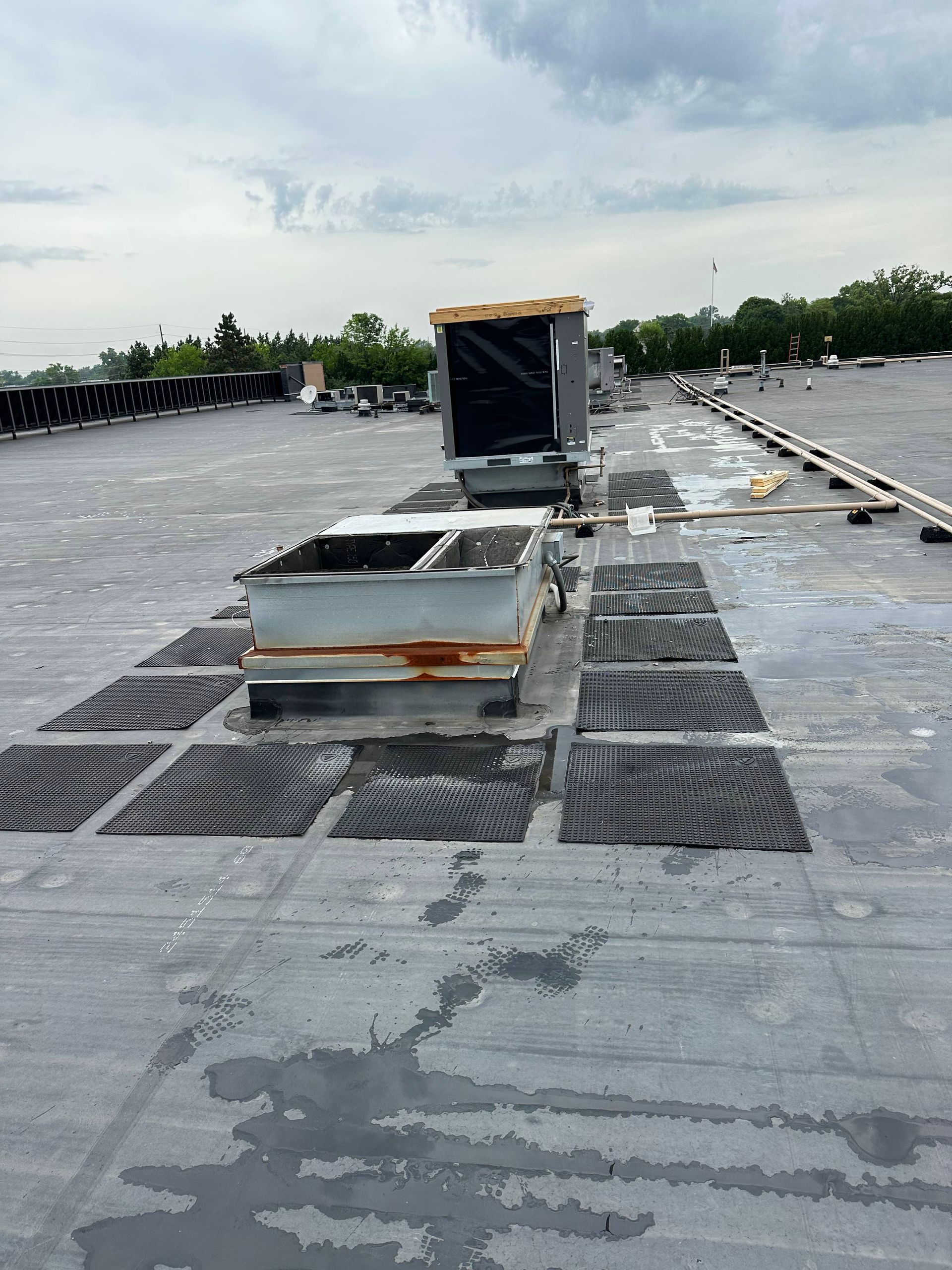 Rooftop HVAC unit on a flat gray roof under a cloudy sky.