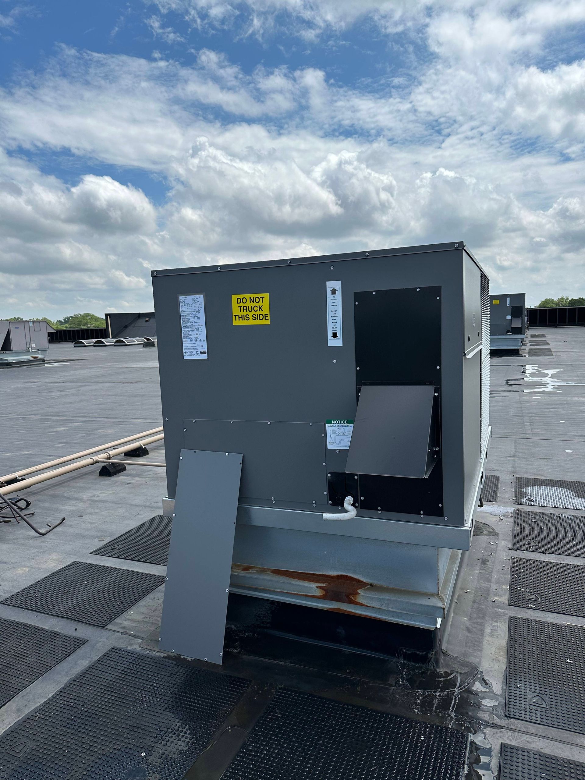 Gray rooftop utility box with open panel door on a cloudy waterfront deck