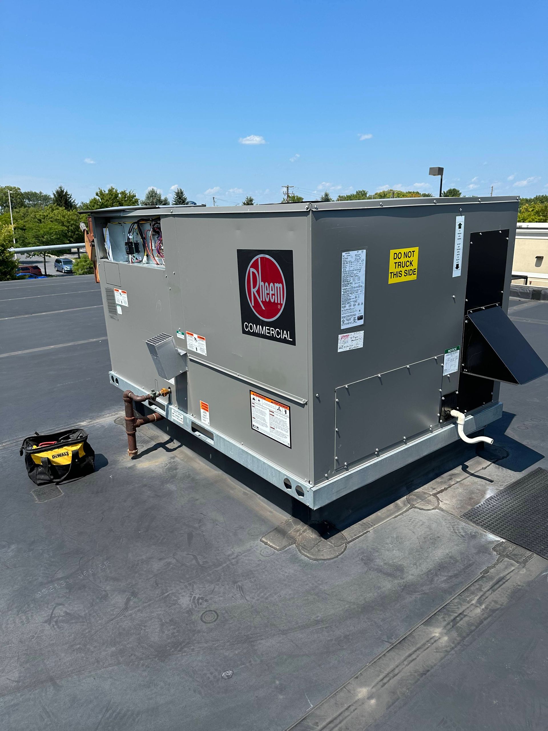 Gray rooftop HVAC unit on a paved lot, with a small yellow tool box beside it under a blue sky