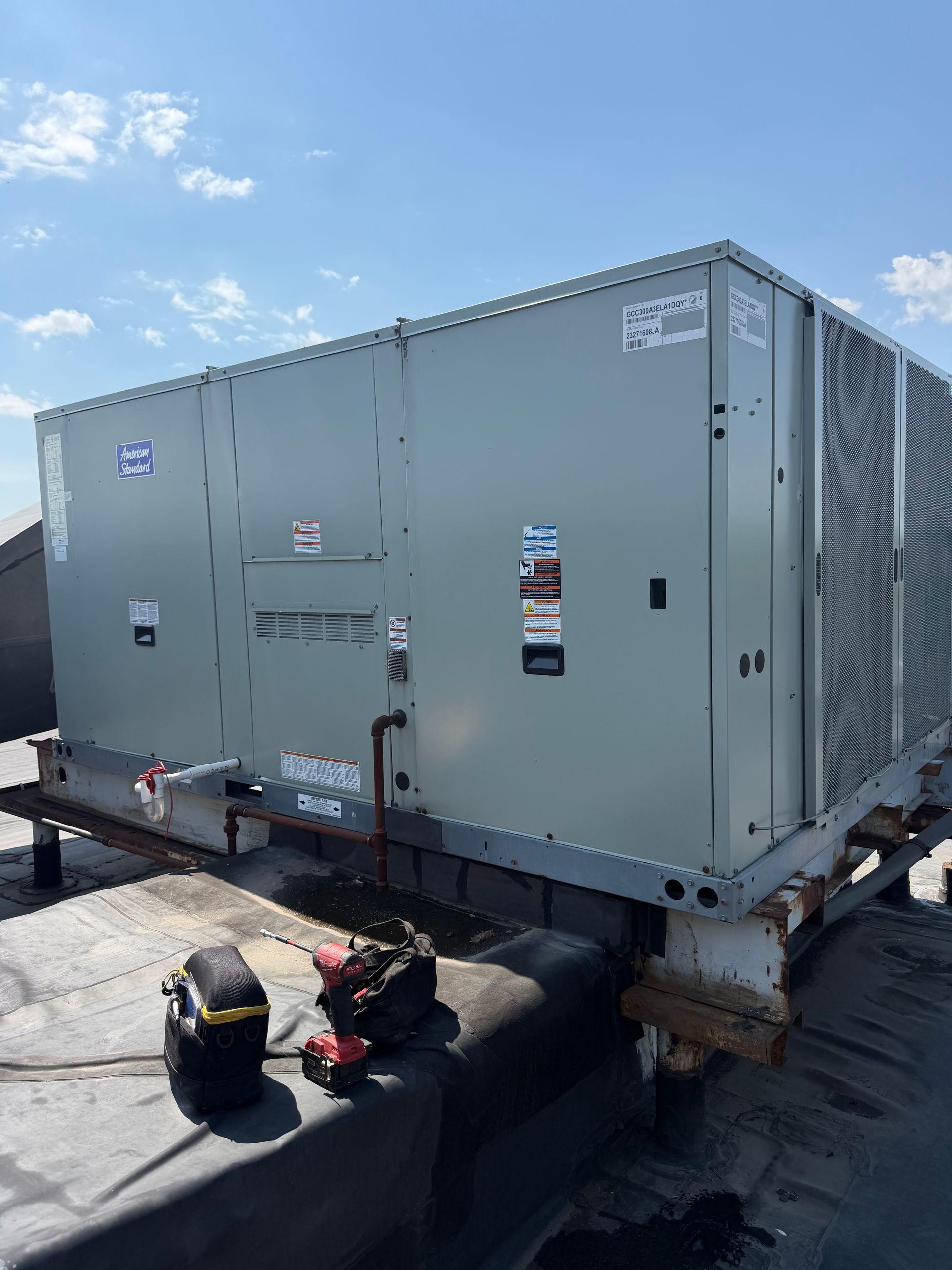 Large gray industrial HVAC unit on a rooftop under a blue sky with a few maintenance tools nearby
