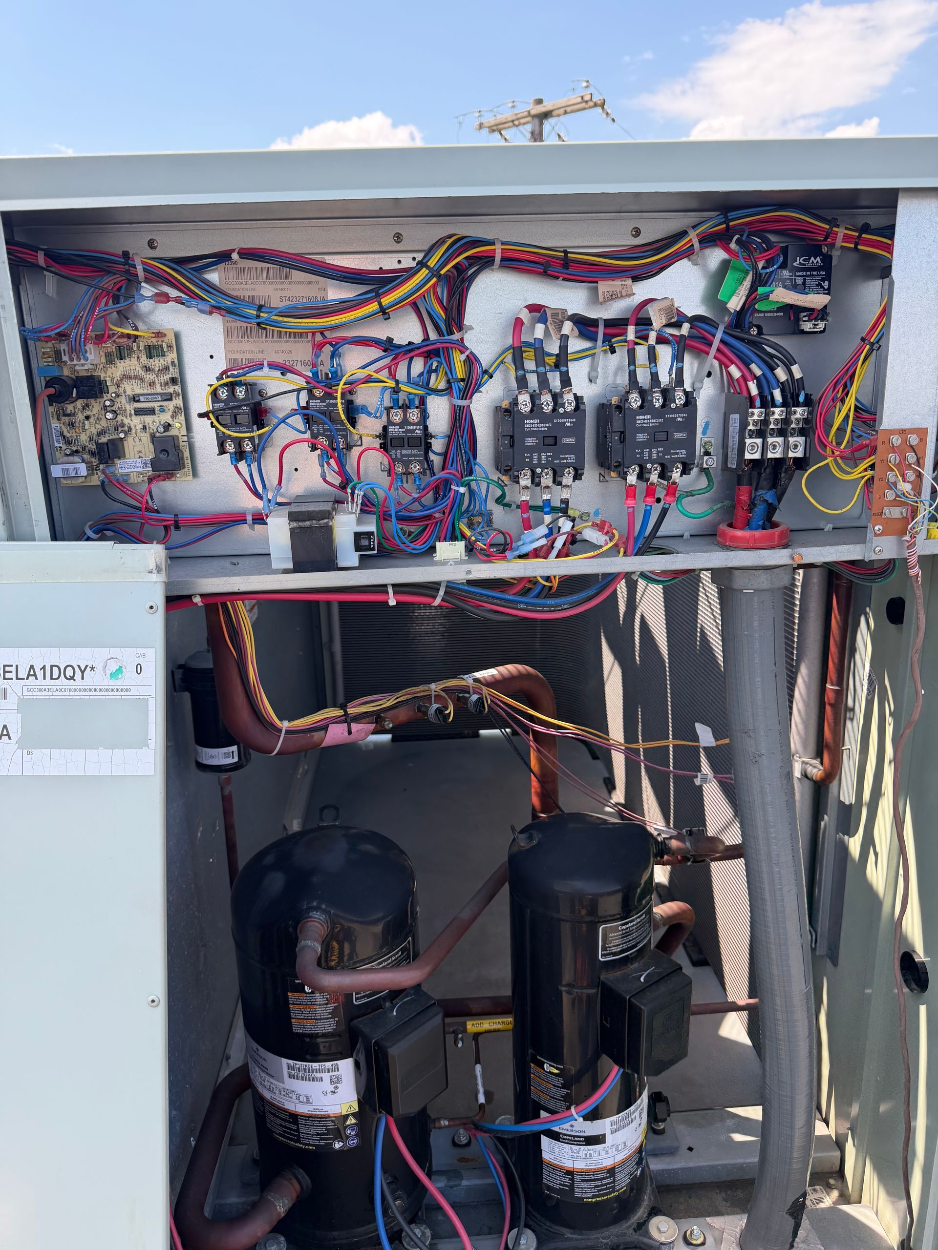 Open electrical panel with tangled multicolored wiring and two black pumps below.
