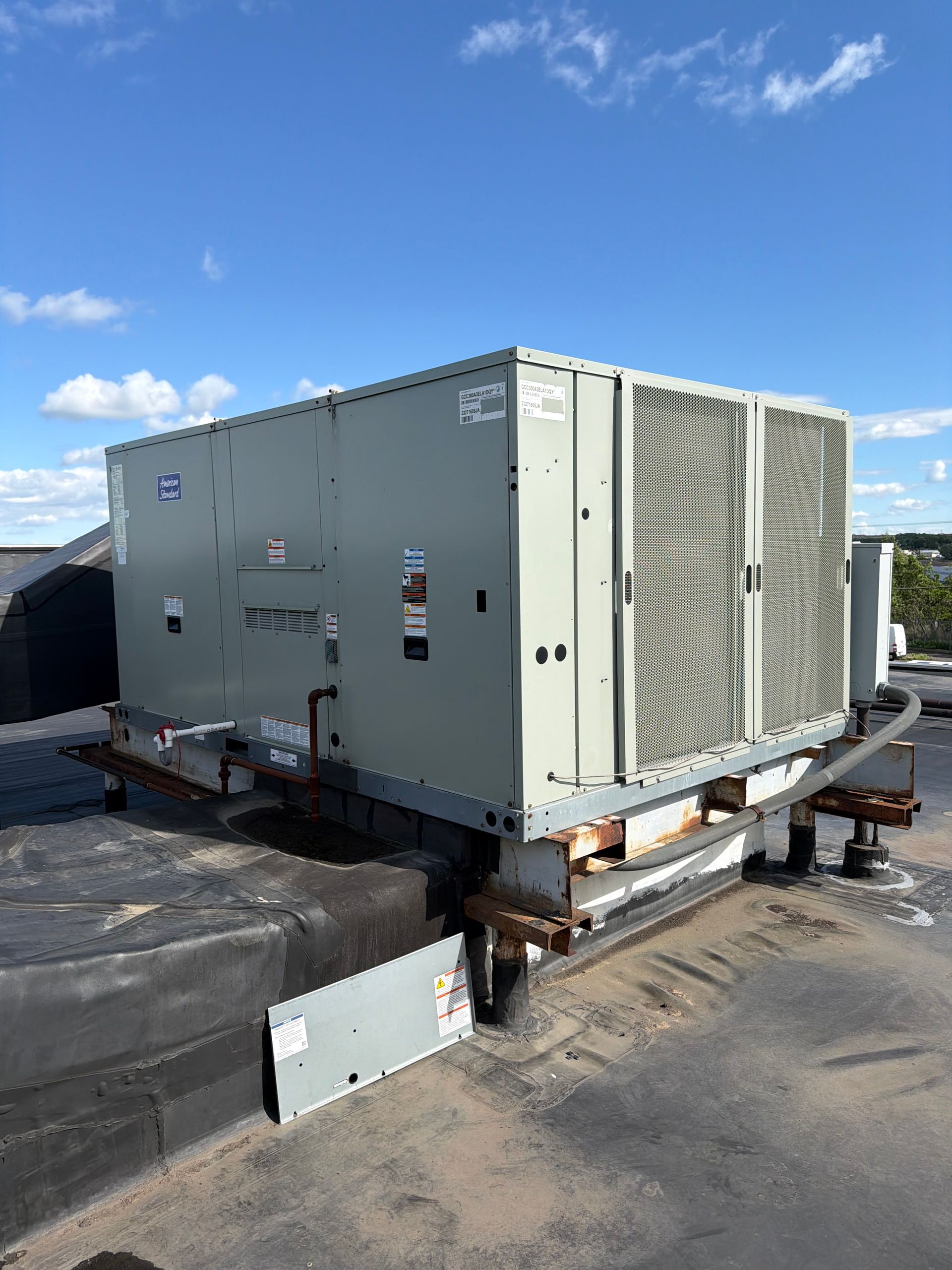 Large beige HVAC unit on a rooftop under a blue sky, with debris and a detached panel nearby