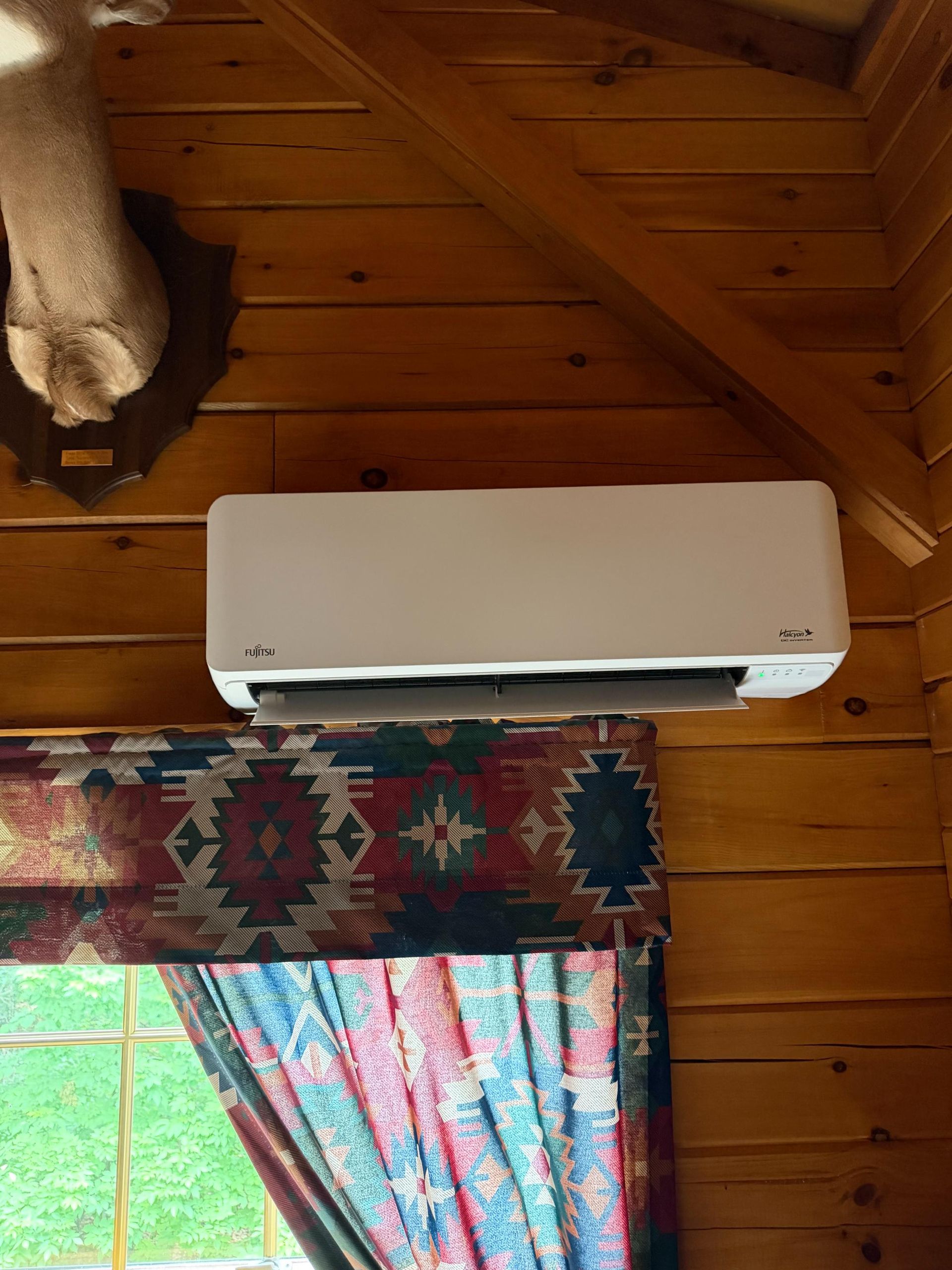 White wall-mounted air conditioner above a patterned curtain in a wood-paneled room