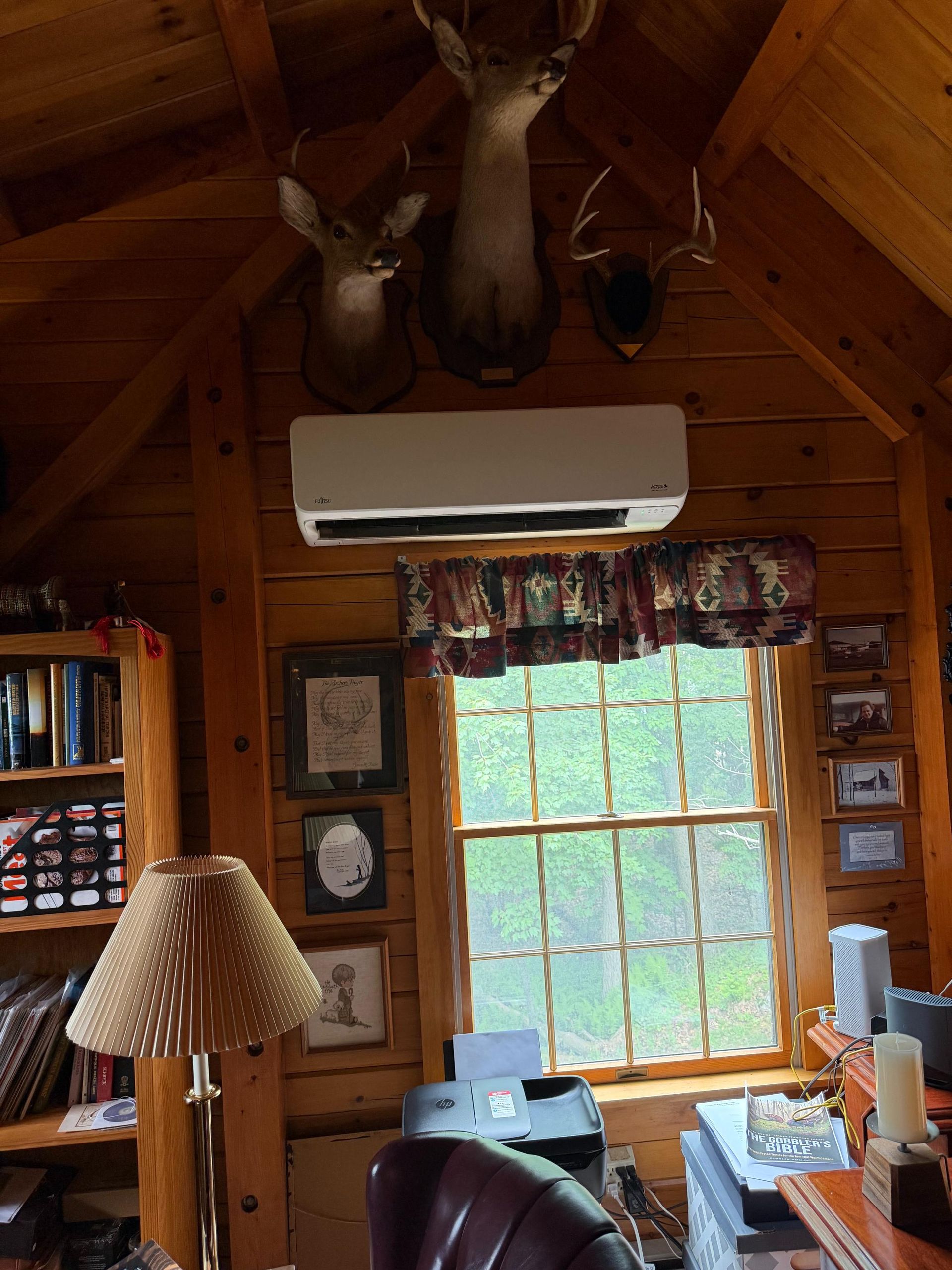 Cozy log cabin interior with wood walls, window, mounted deer heads, and an air conditioner above the window
