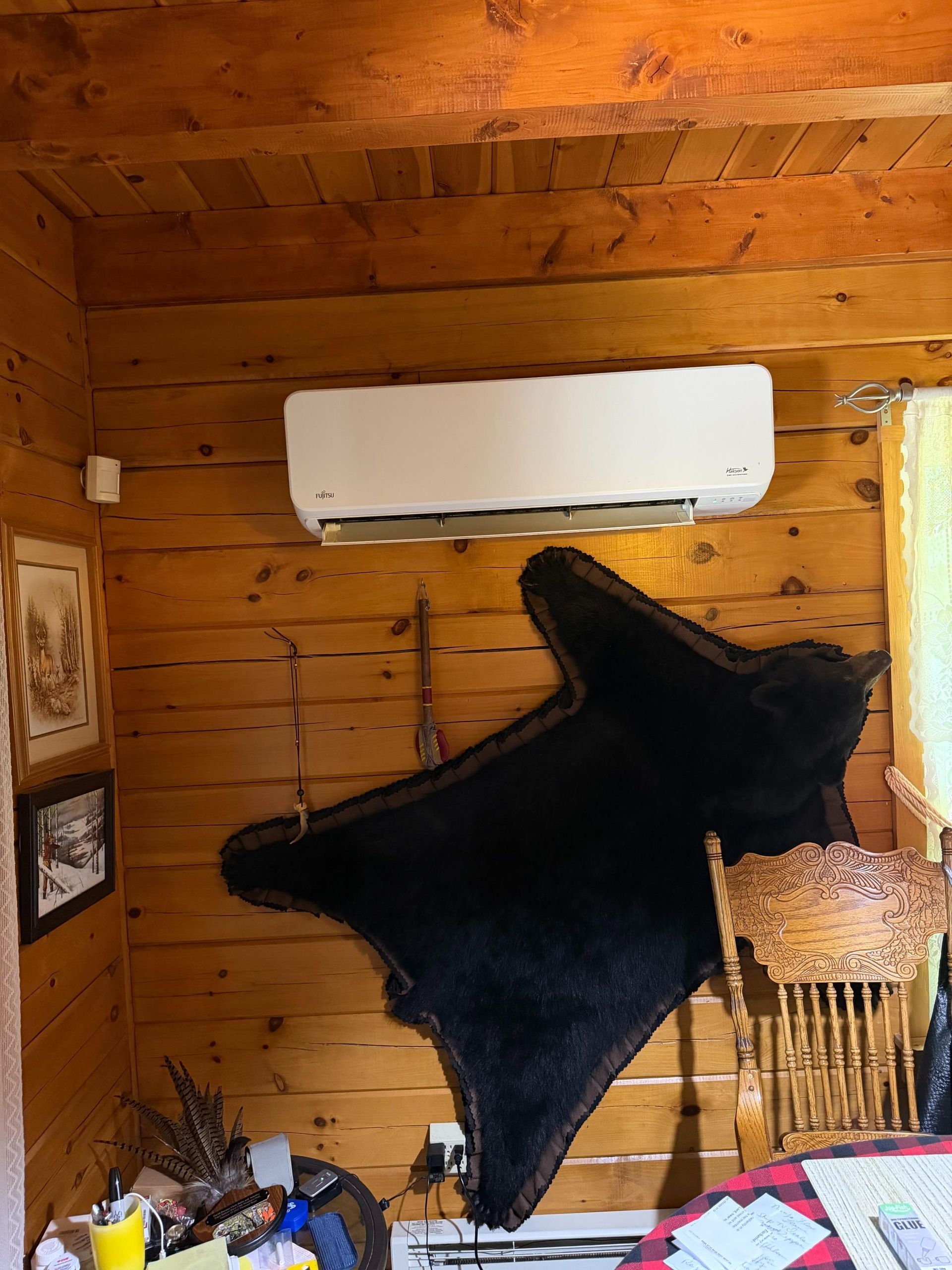 Black fur rug or hide hanging on a wooden wall beneath a white air conditioner.