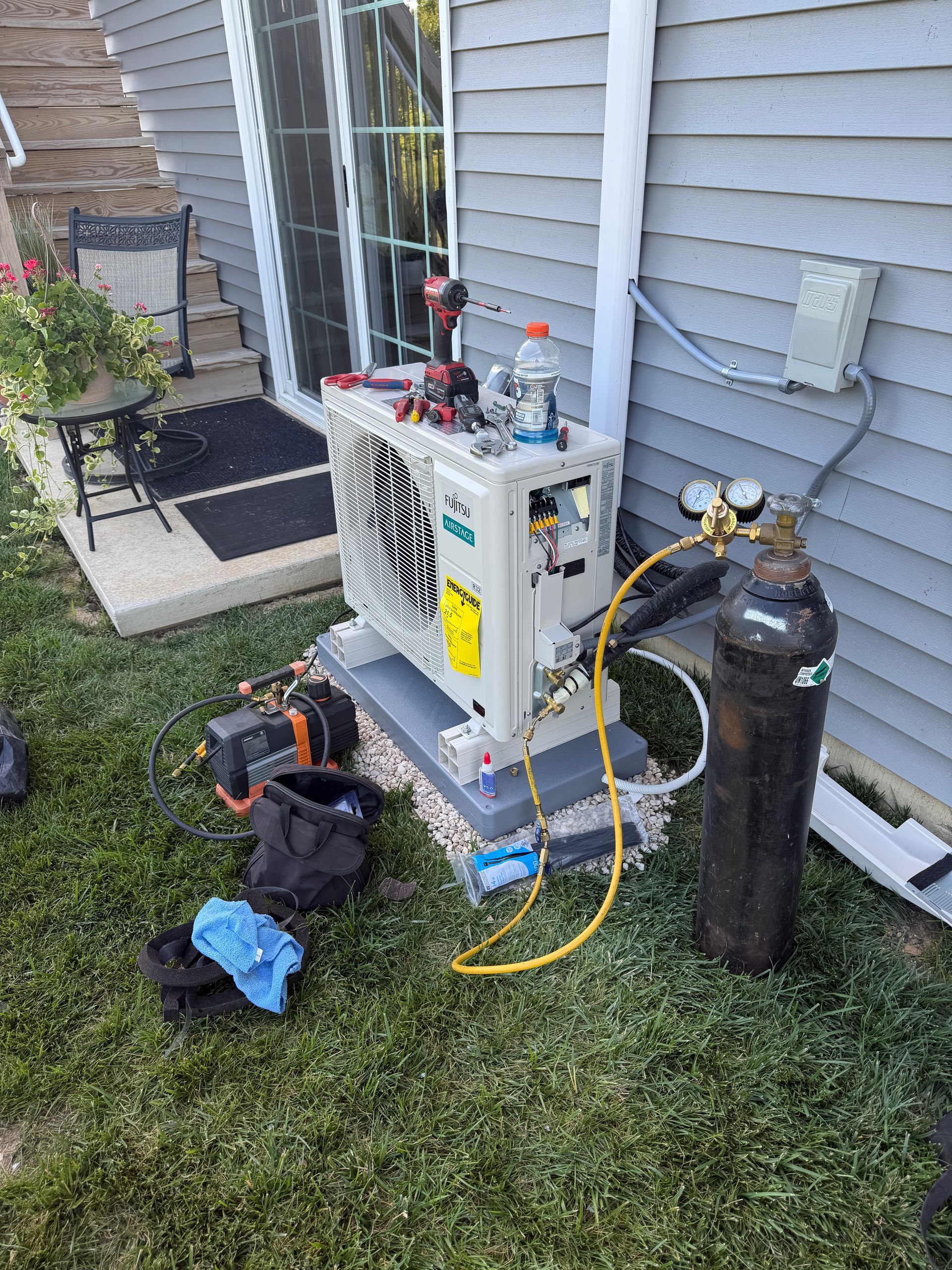 An air conditioning unit is installed near a building's wall, with electrical connections and service tools nearby.