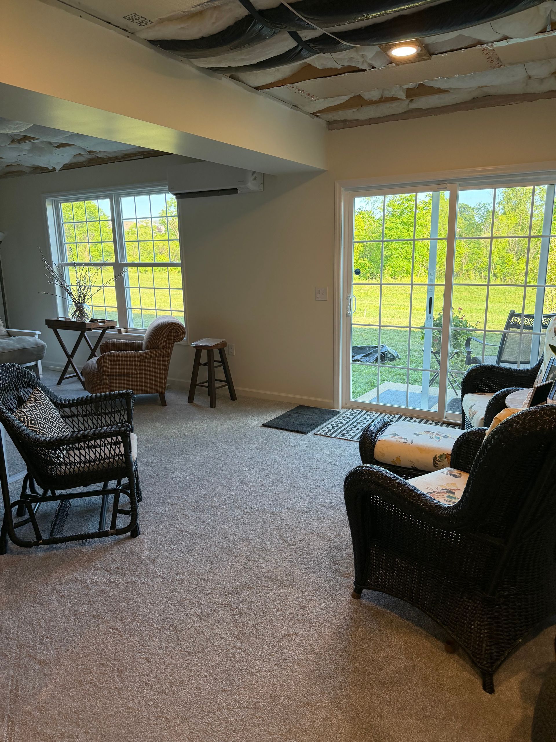 Bright living room with wicker chairs, carpeted floor, and large sliding glass doors overlooking trees