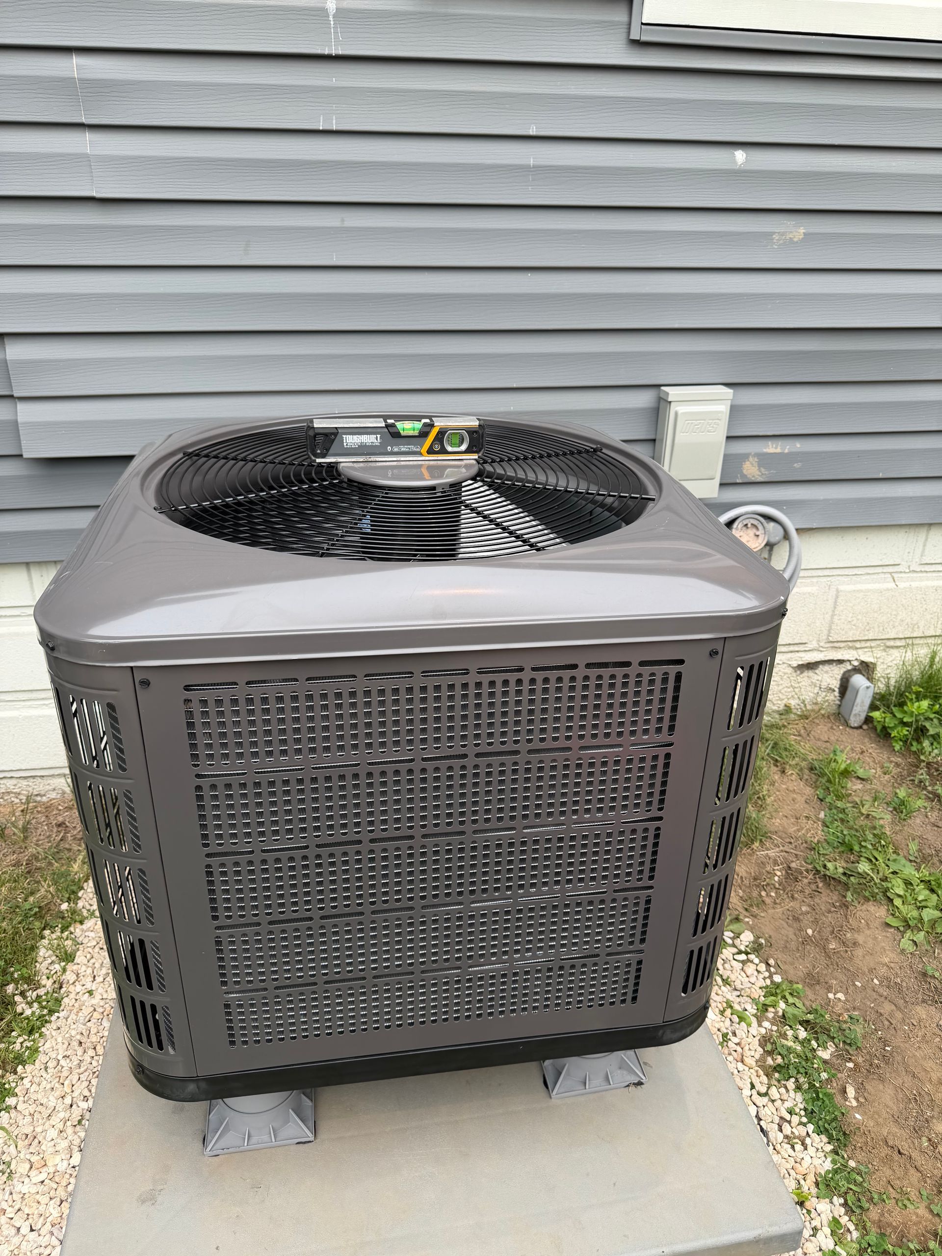 Outdoor HVAC unit on a concrete pad beside a gray house wall