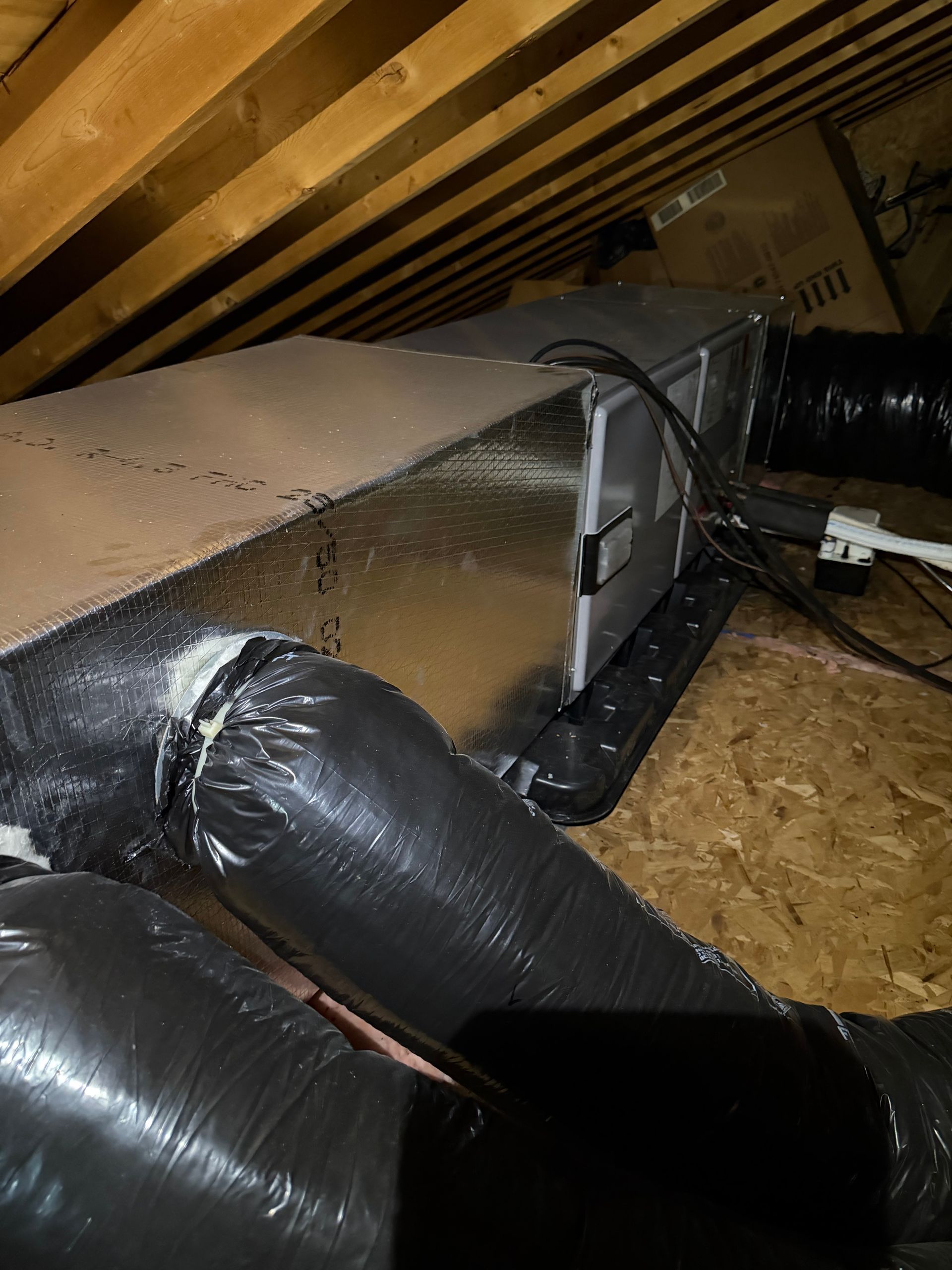 Insulated attic HVAC ducts beneath a sloped roof with exposed wooden framing