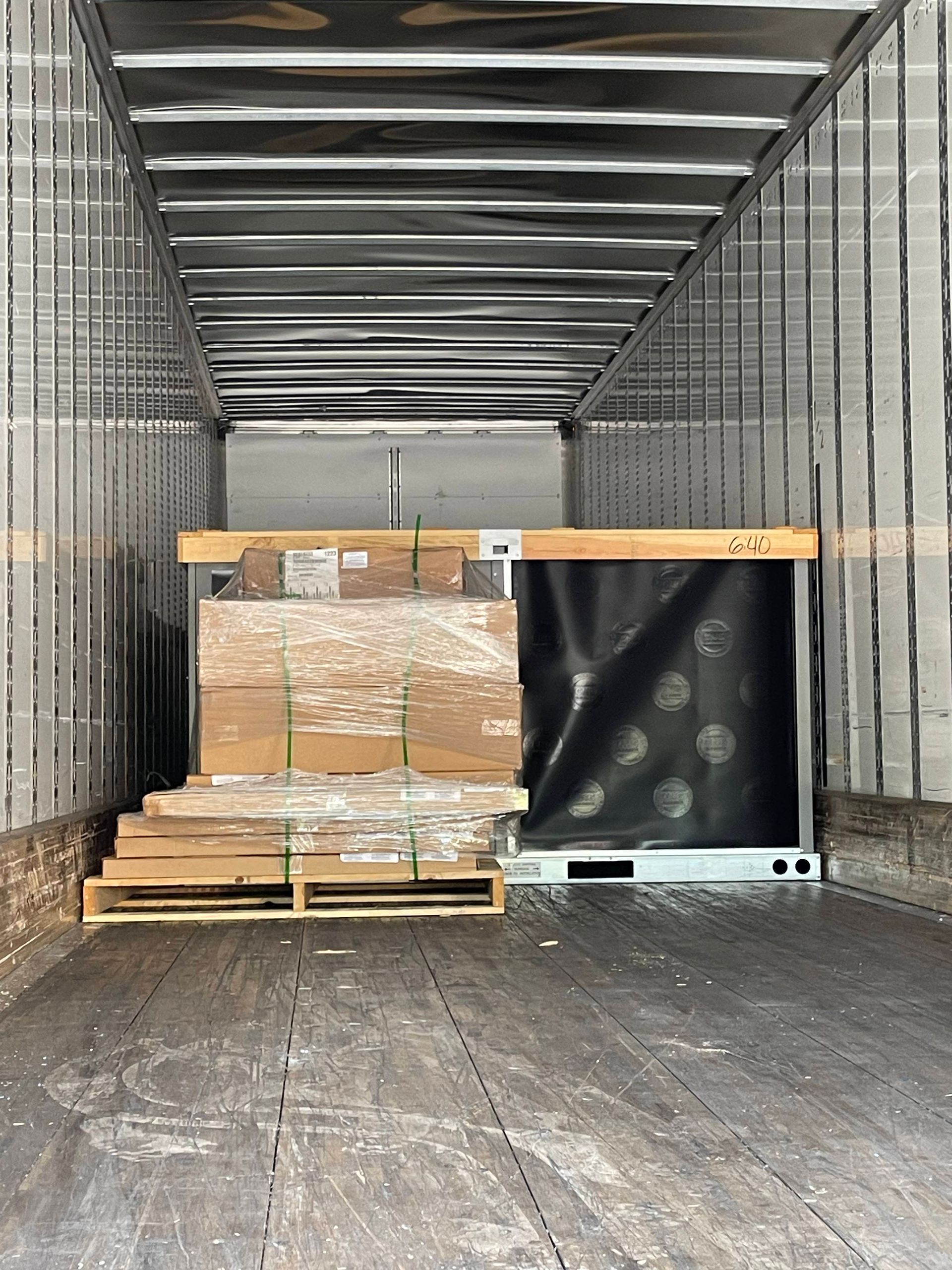 Empty cargo trailer with a palletized stack of boxes and wood secured near the front.