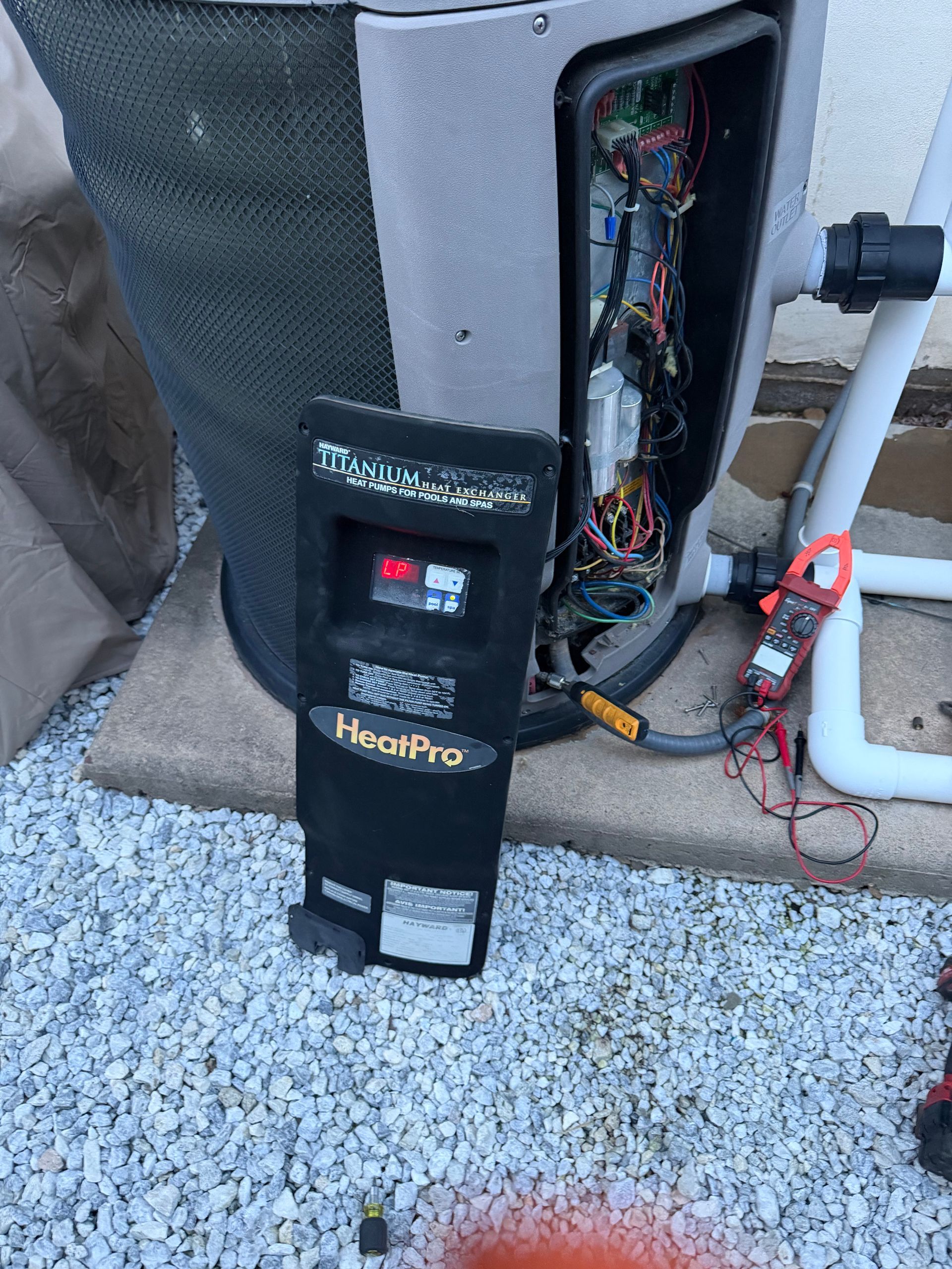 Damaged HeatPro pool heater with open side panel and exposed wiring beside a swimming pool.