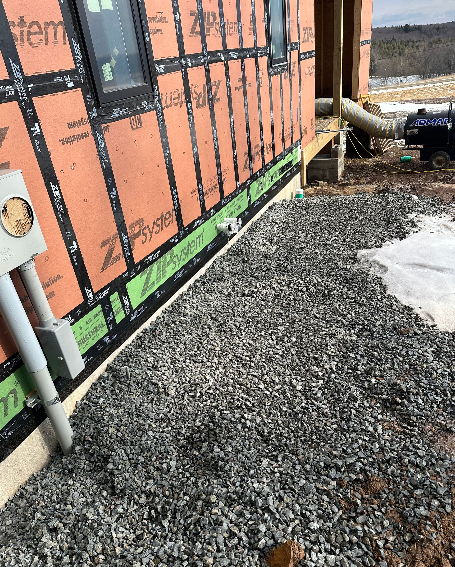 Exterior wall with gravel bed, electrical box, black wrap, and green flashing.