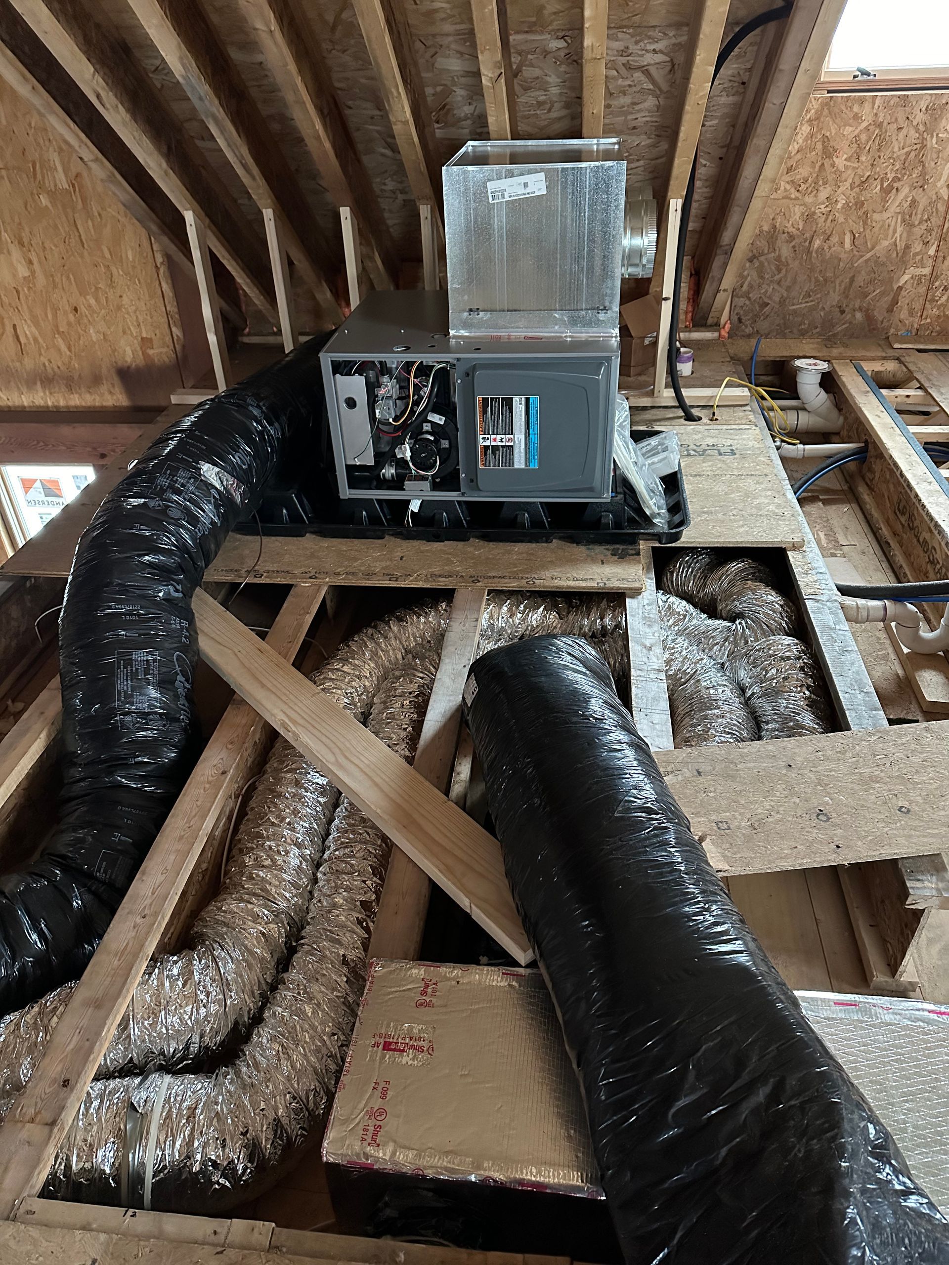 HVAC unit in an attic space, with ductwork snaking through wooden beams.