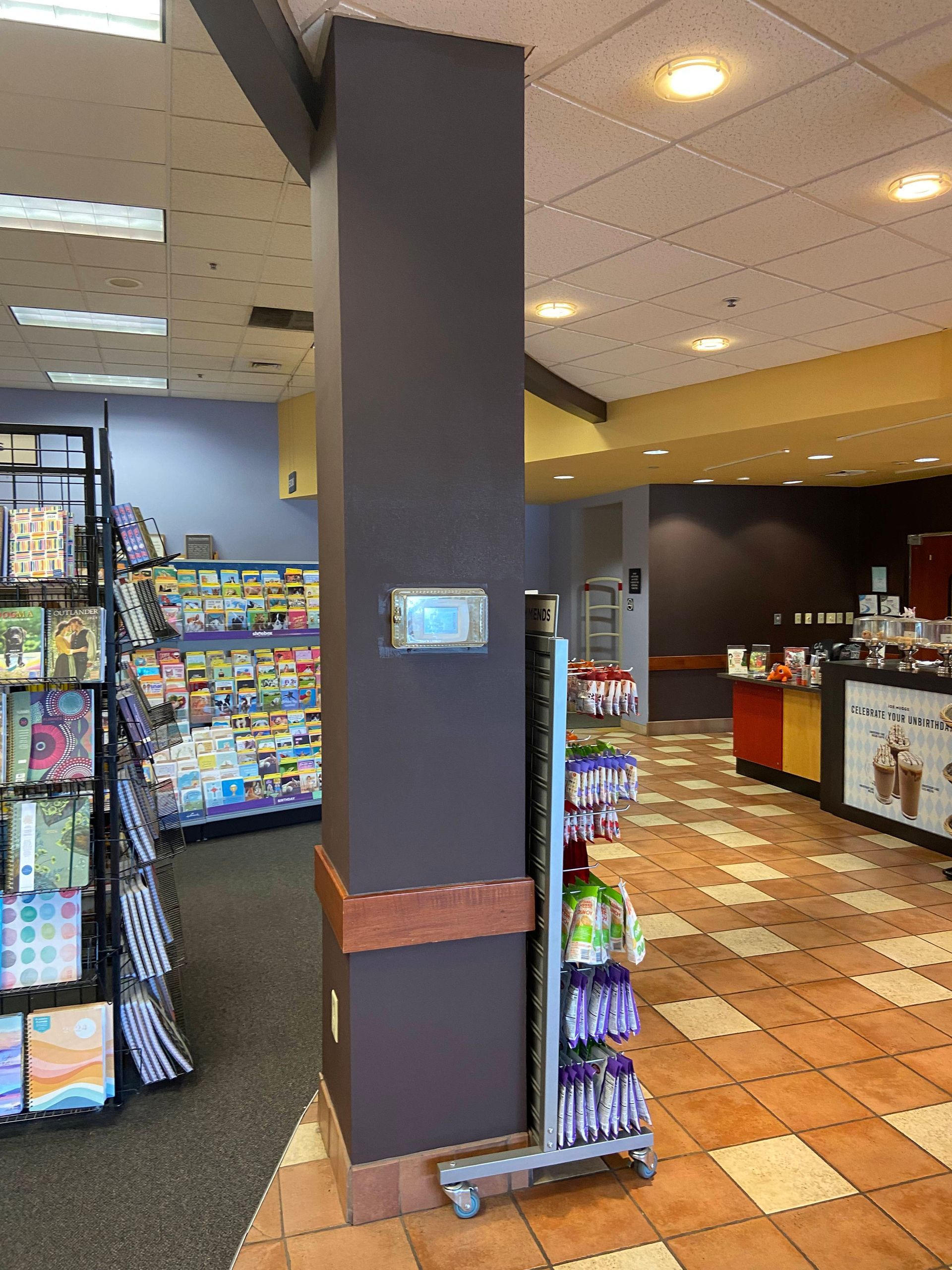 Convenience store interior with snack racks, tiled floor, and a central pillar-mounted touchscreen kiosk