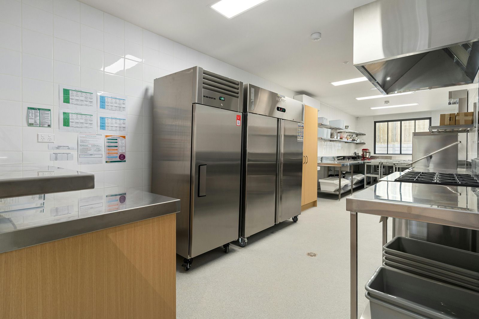Commercial kitchen with stainless steel refrigerators, countertops, and cooking equipment.