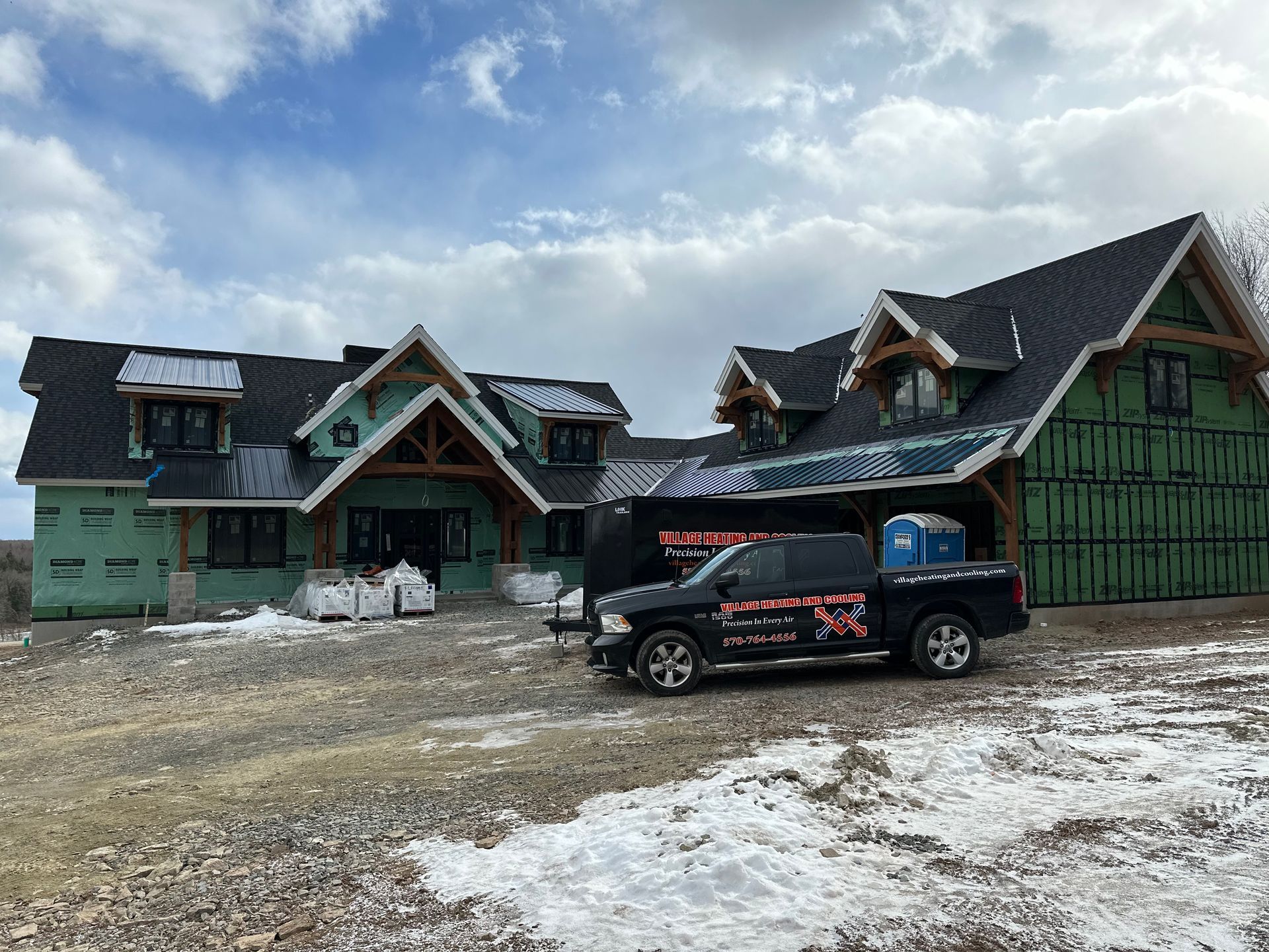 New home under construction with black roof and a truck in front, with snow.
