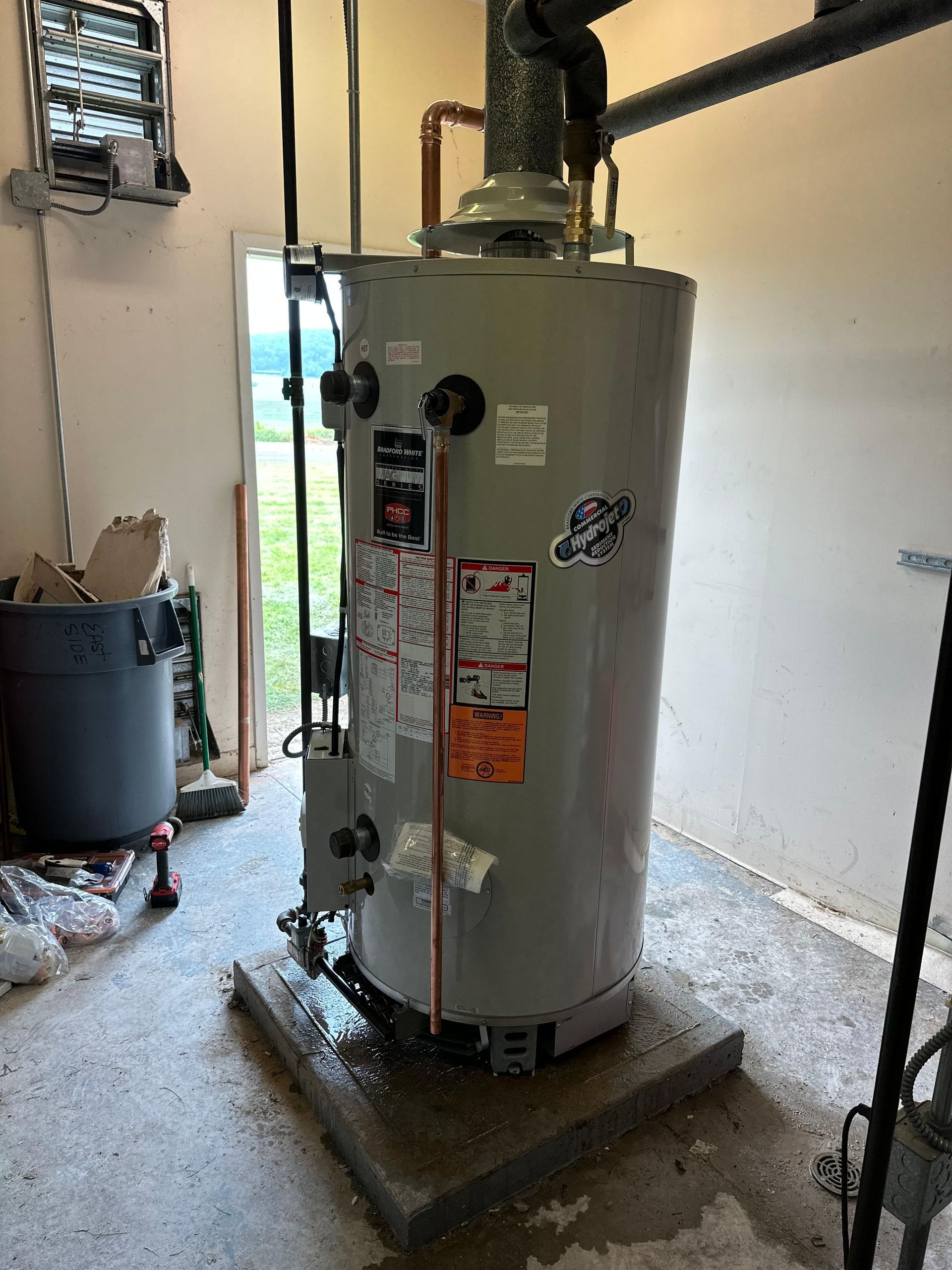 Water heater in a garage, surrounded by water, with pipes and controls visible.