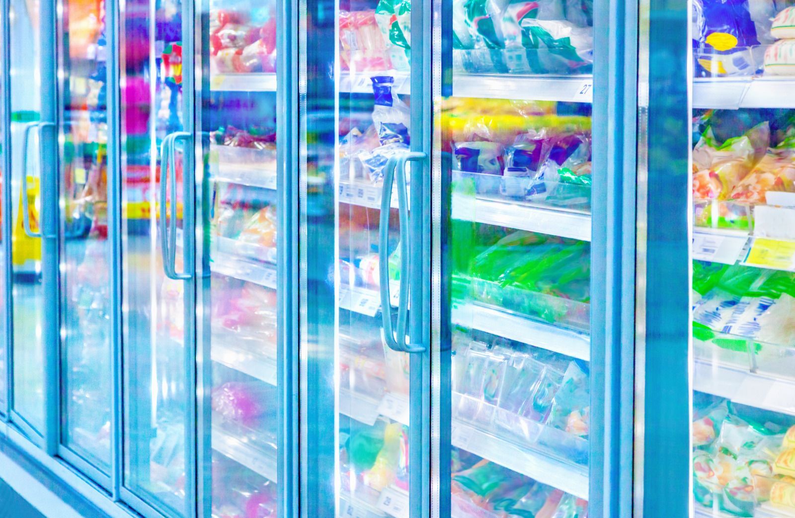 Freezer doors in a store, filled with colorful frozen food products. Blue and white tones.