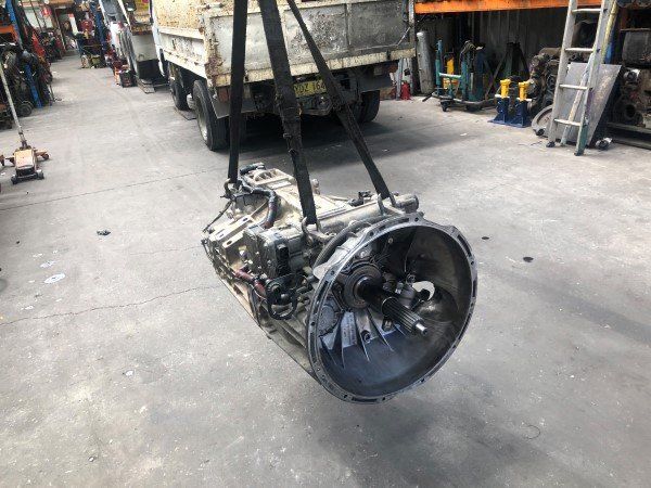 A gearbox is hanging from a crane in a garage.