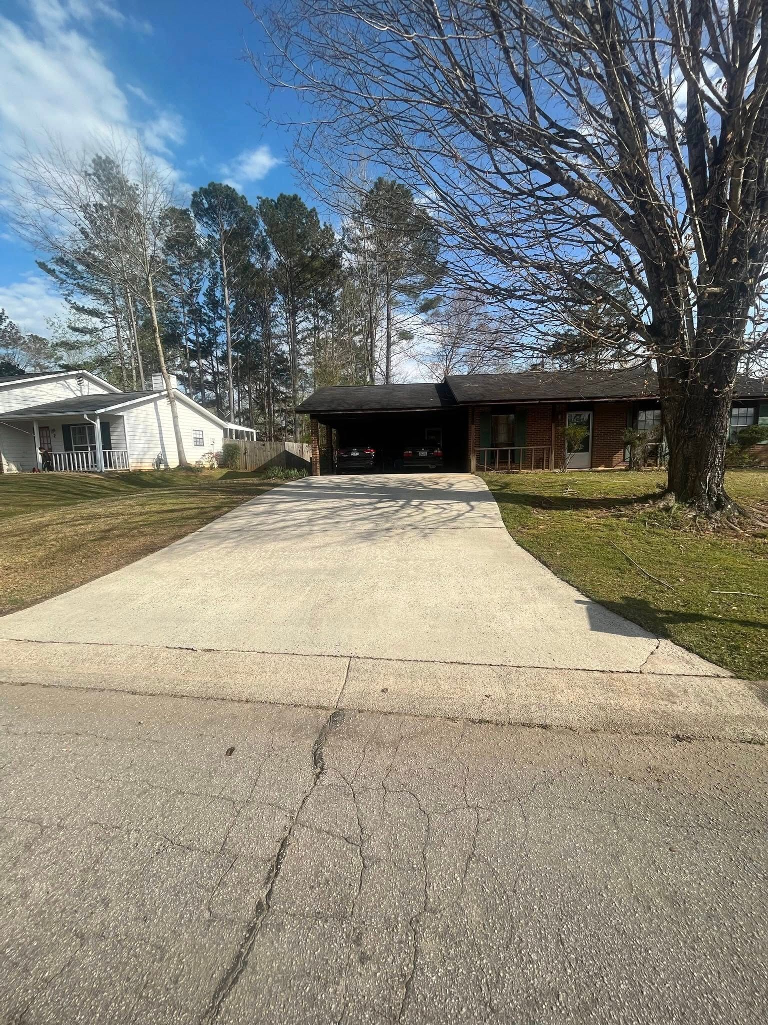 Residential driveway leading to a single-story house with trees and blue sky