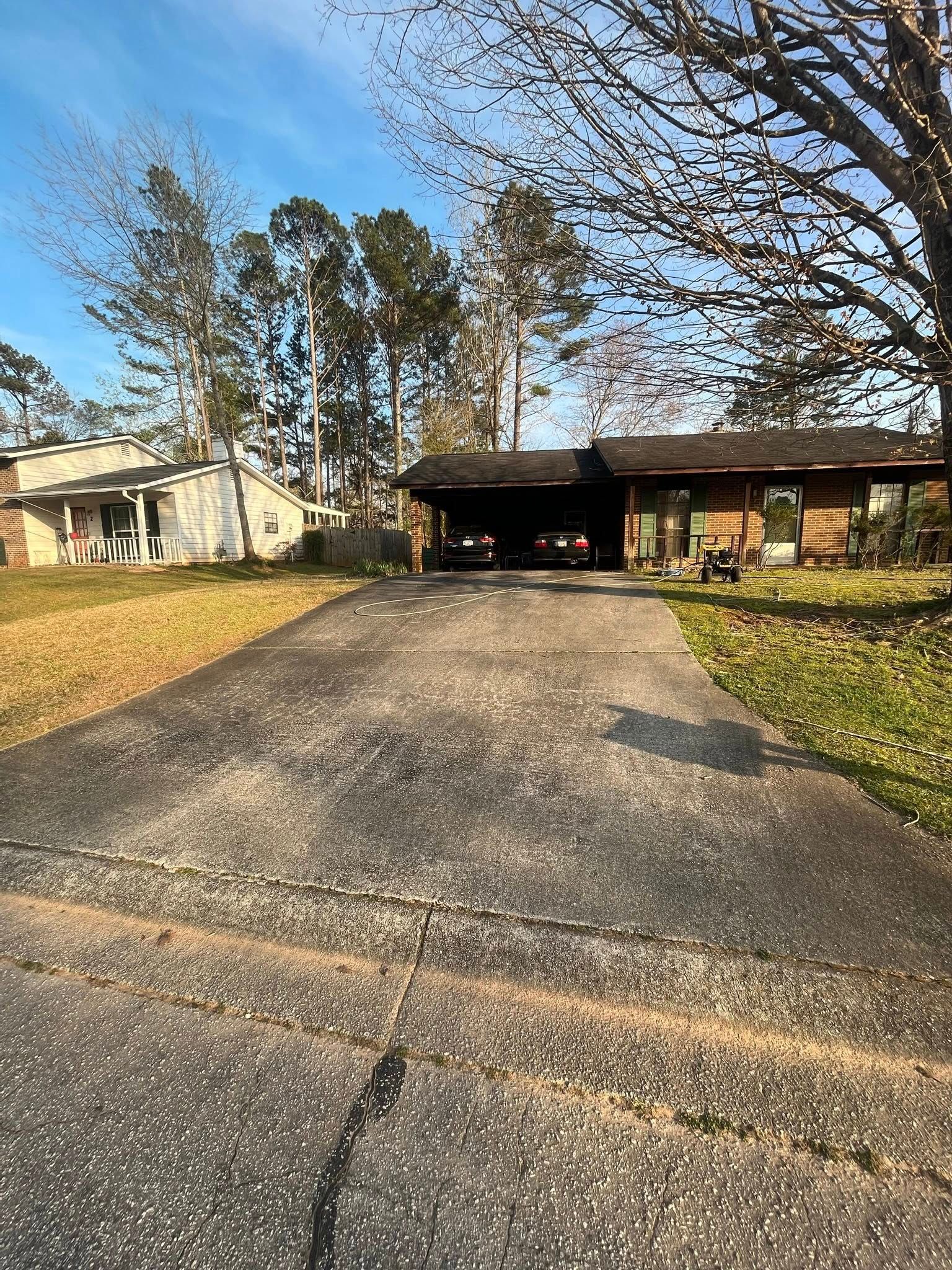 Driveway leading to a suburban home with trees and a carport under a clear blue sky.
