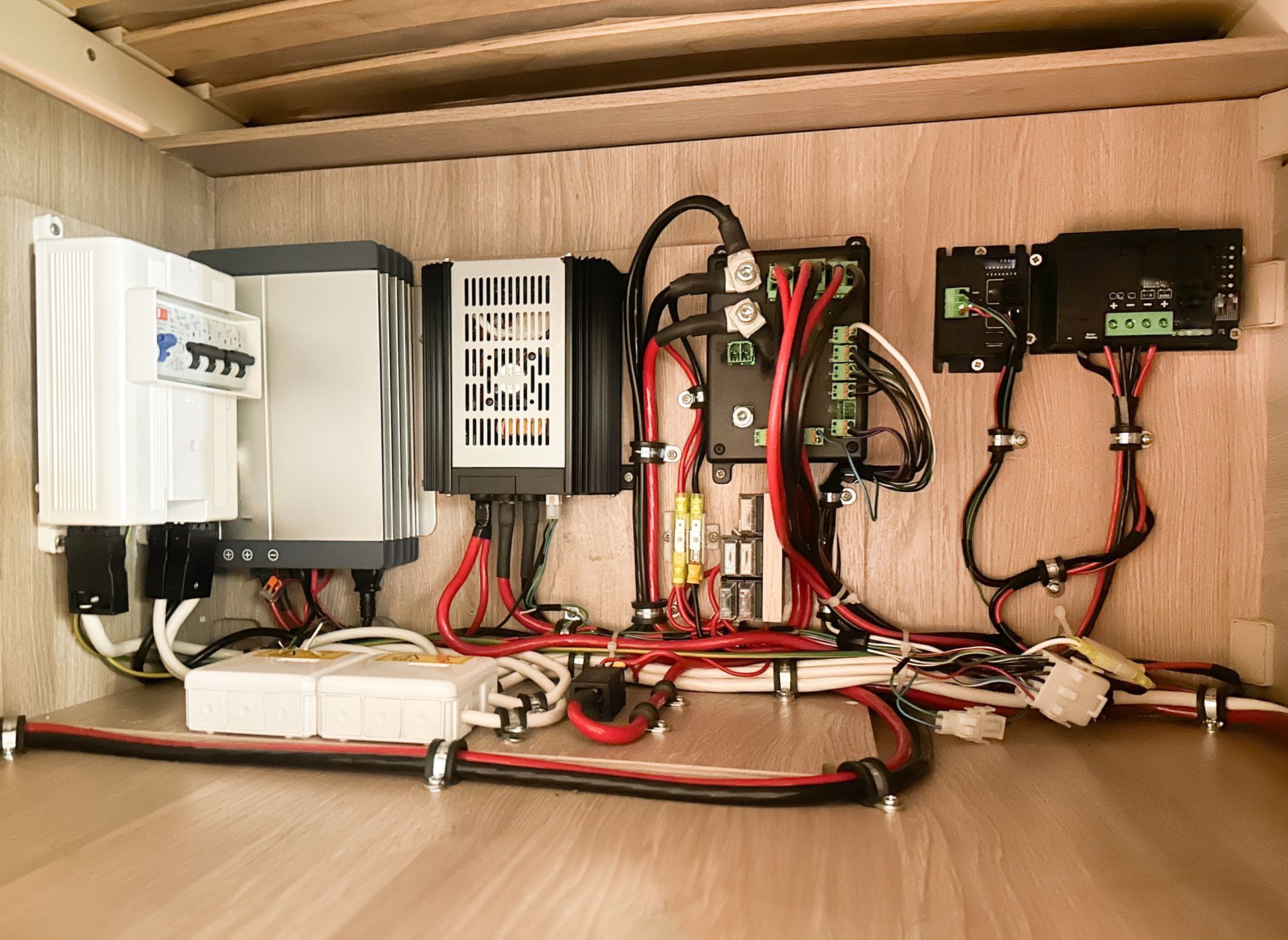 Electrical equipment and complex wiring mounted on a wooden wall inside an RV storage compartment.