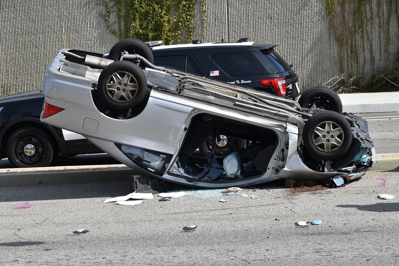 Silver car overturned on asphalt, next to a police SUV. Debris scattered around the scene.
