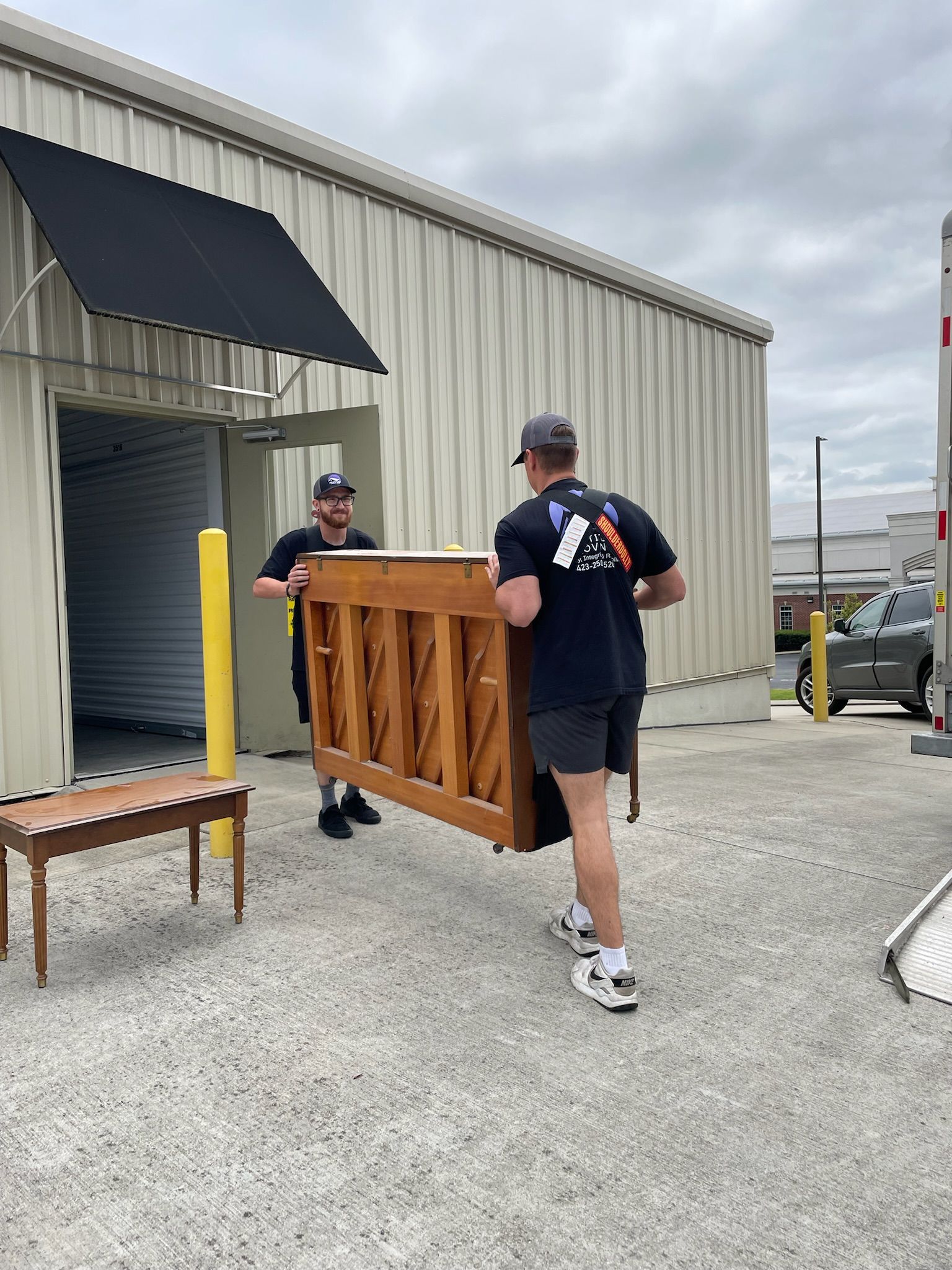Two men are carrying a piano in front of a building.