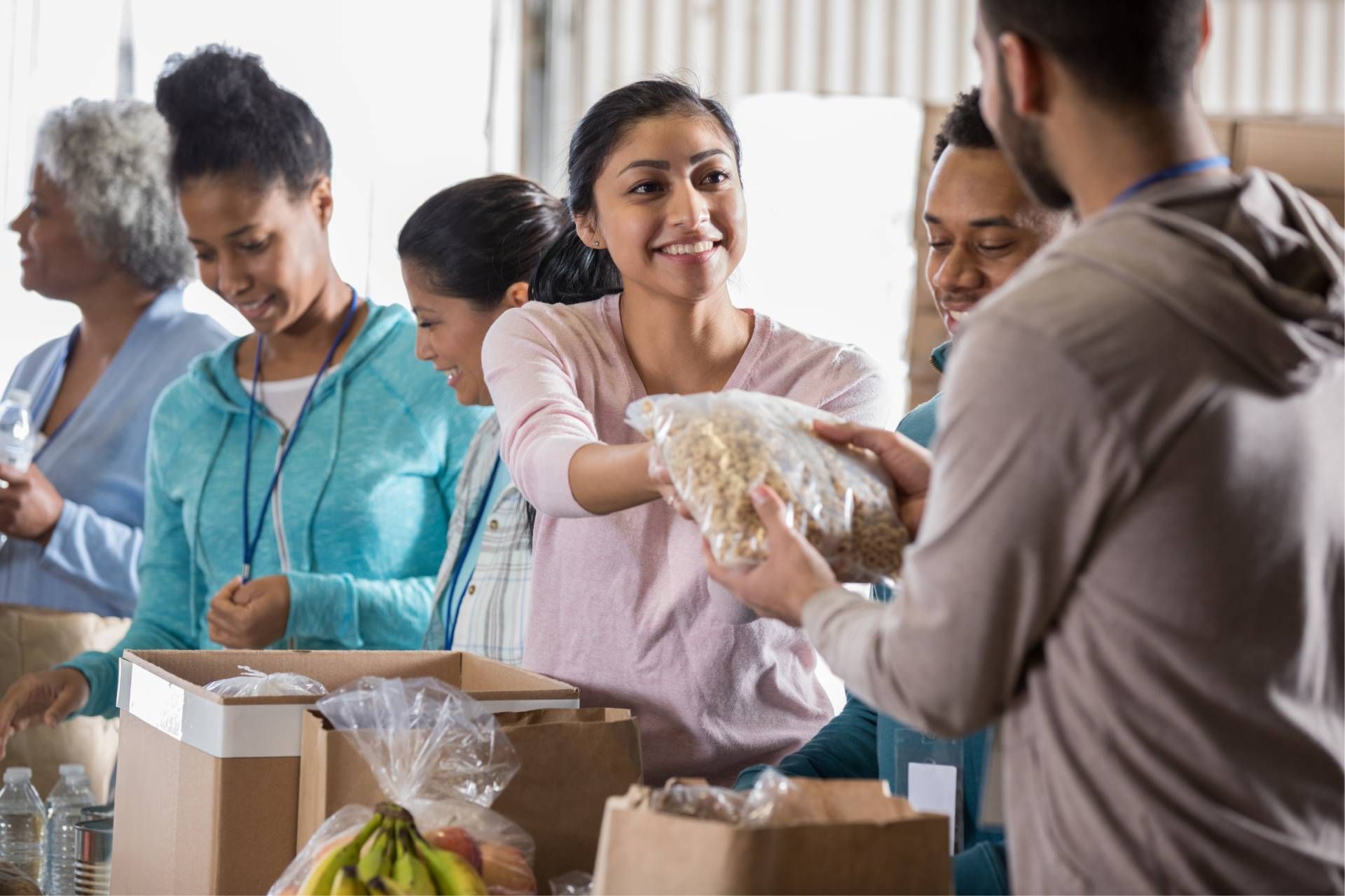 Volunteers pack food at a distribution center, passing bags and boxes.