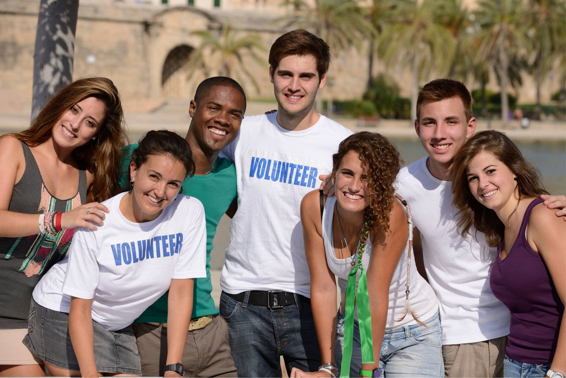 Group of volunteers smiling outdoors in front of a building and water.