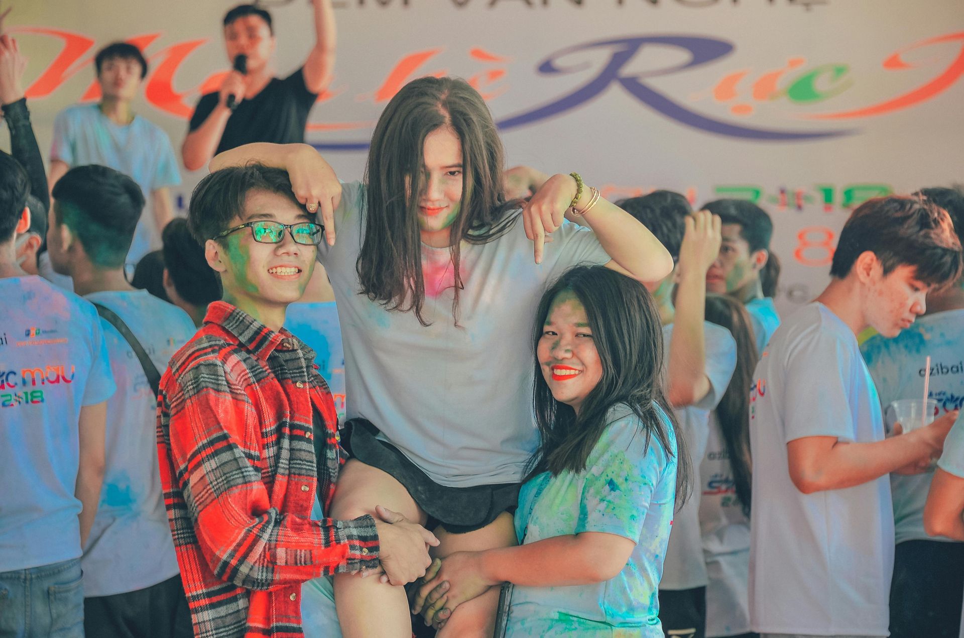 People at a festival, covered in colored powder, pose for photo. One person is held aloft.