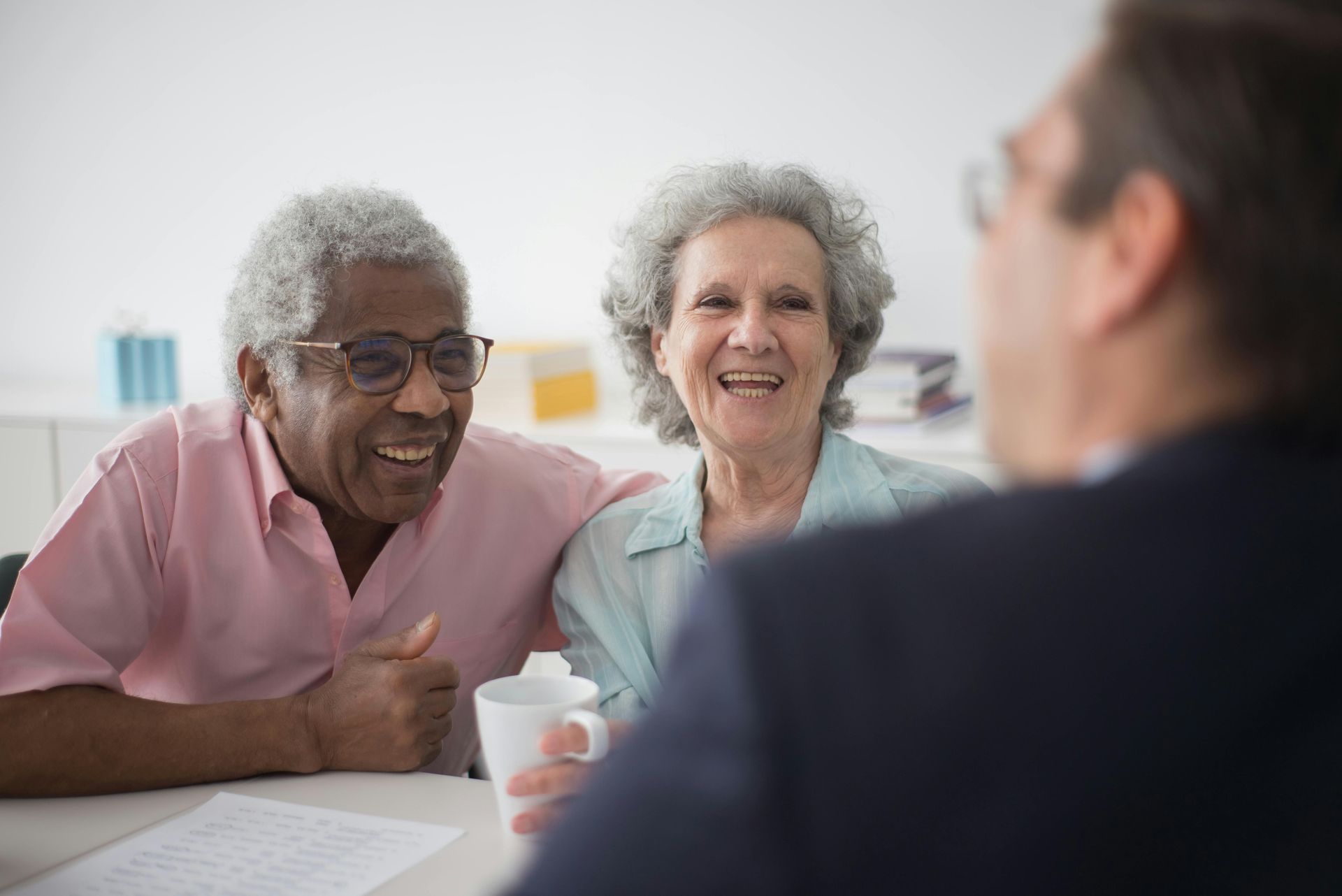 Smiling couple at a table, facing a person out of frame, in an office setting.