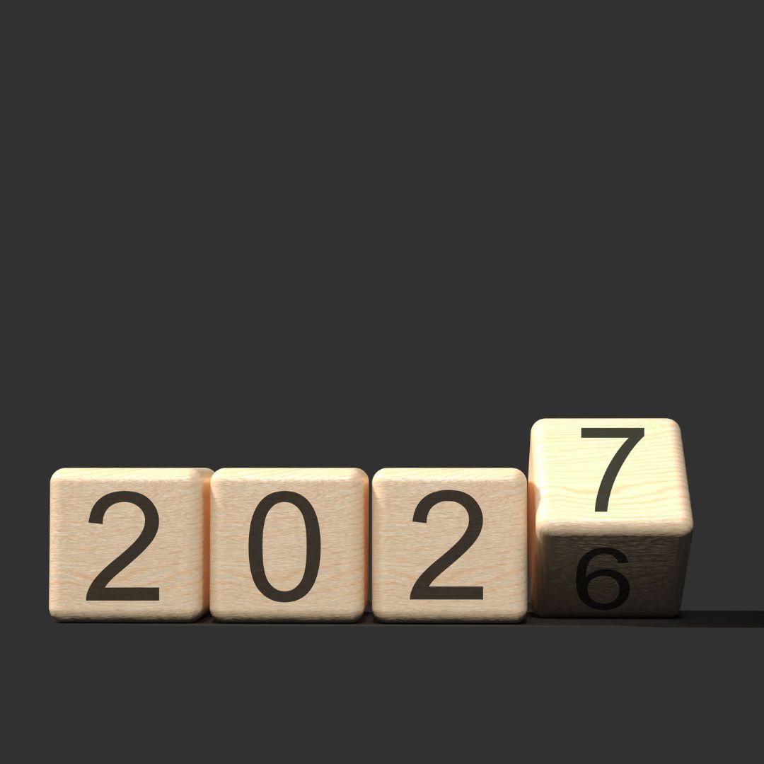 Wooden blocks spelling 2026 on a dark background, with the last block showing 7 over 6.