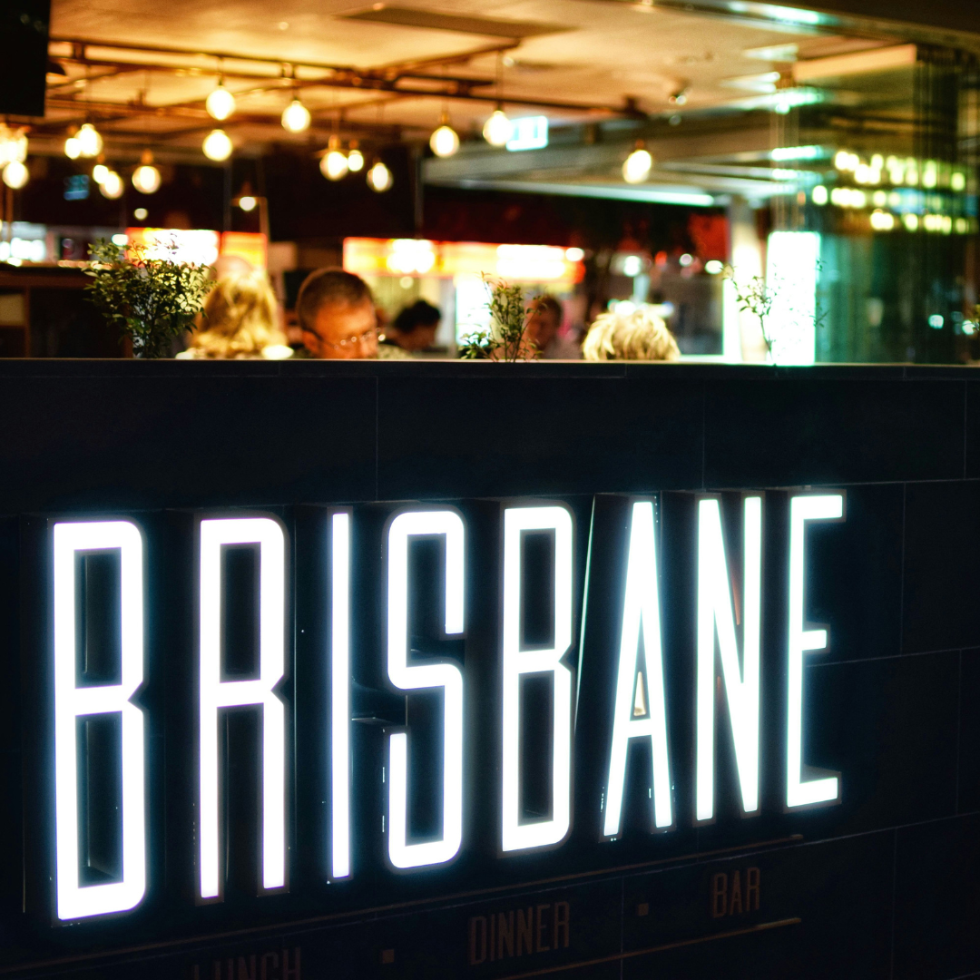 Bright neon sign reading “BRISBANE” inside a warmly lit bar or restaurant
