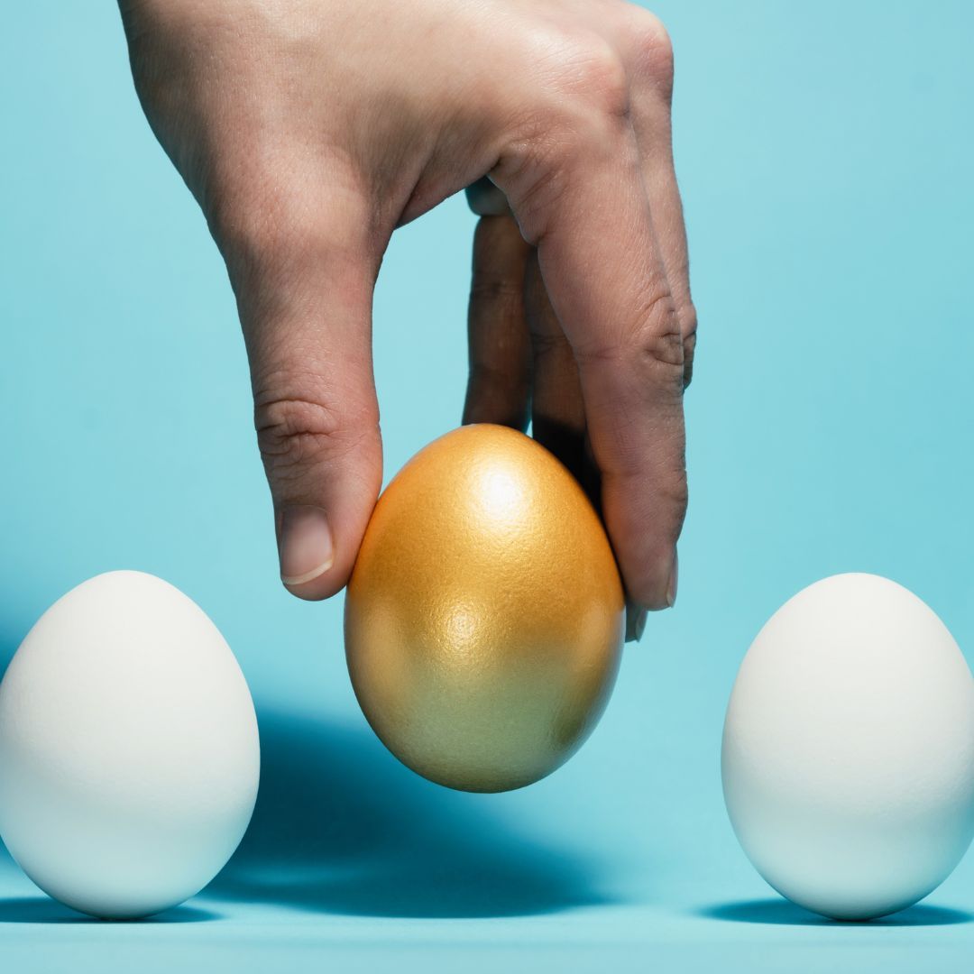 Hand placing a gold egg between two white eggs on a blue background